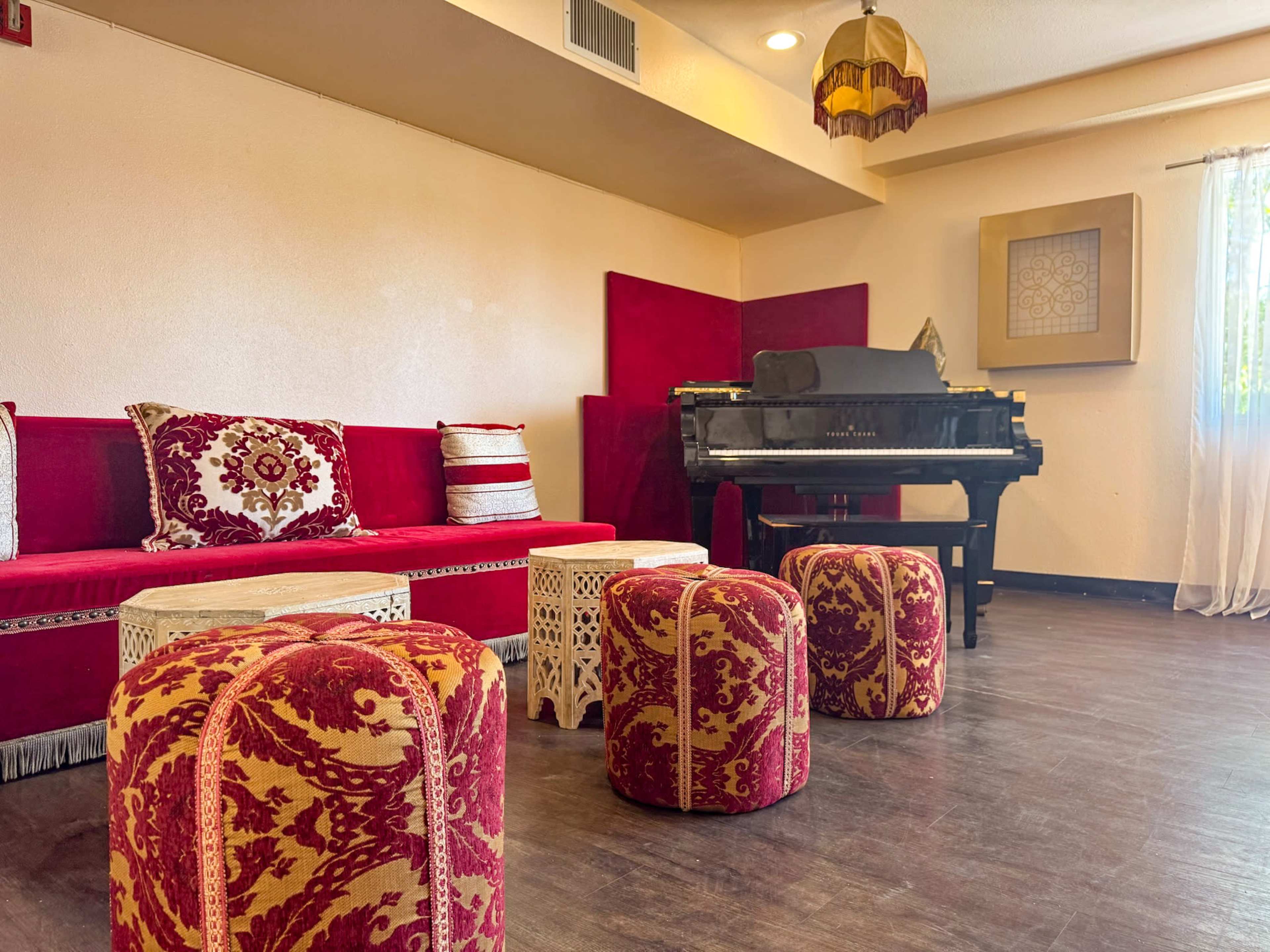 The image shows a room with red and gold decorative furniture, including a plush sofa and patterned stools, along with a black piano in the corner.