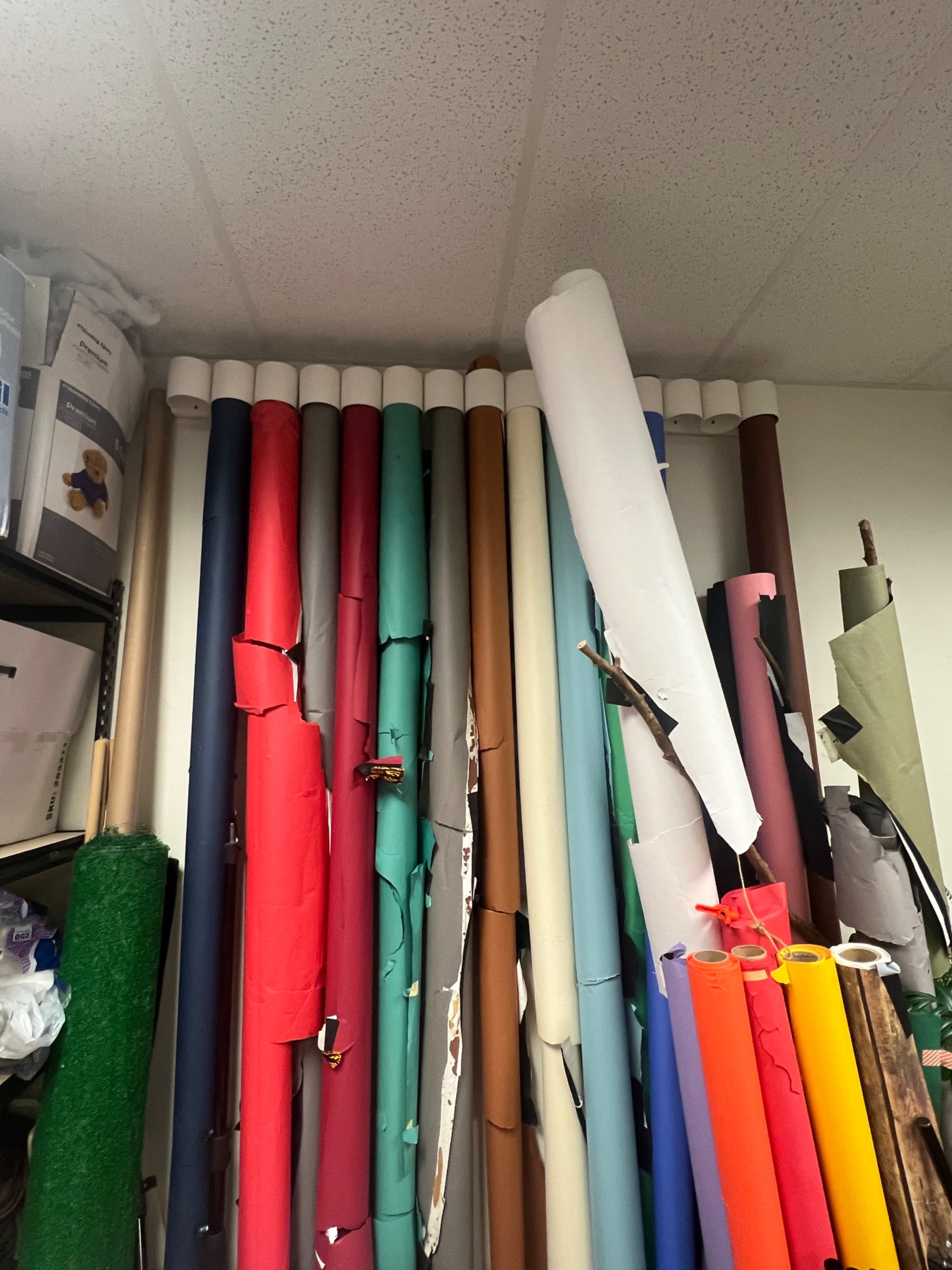A collection of colorful rolls of paper is stacked against a wall, with some rolls partially unwrapped and others displaying visible wear.