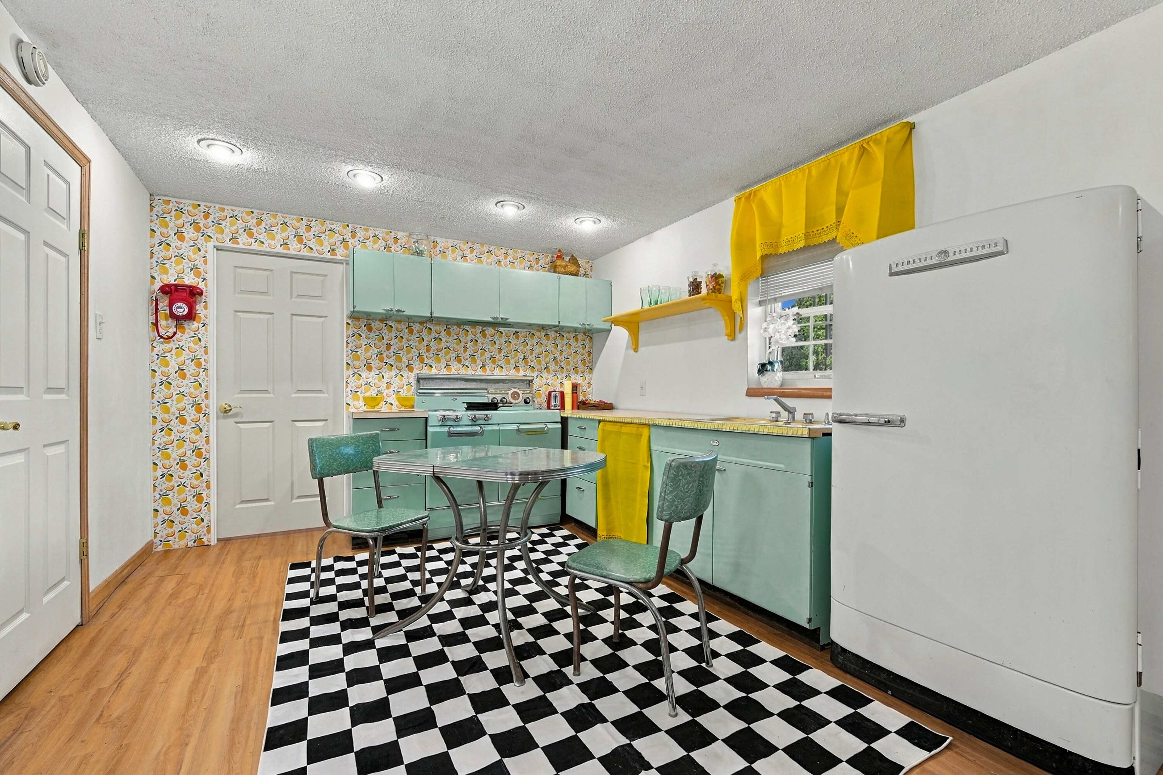 The kitchen features mint green cabinets, a retro-style white refrigerator, a glass dining table, and a black-and-white checkered floor.