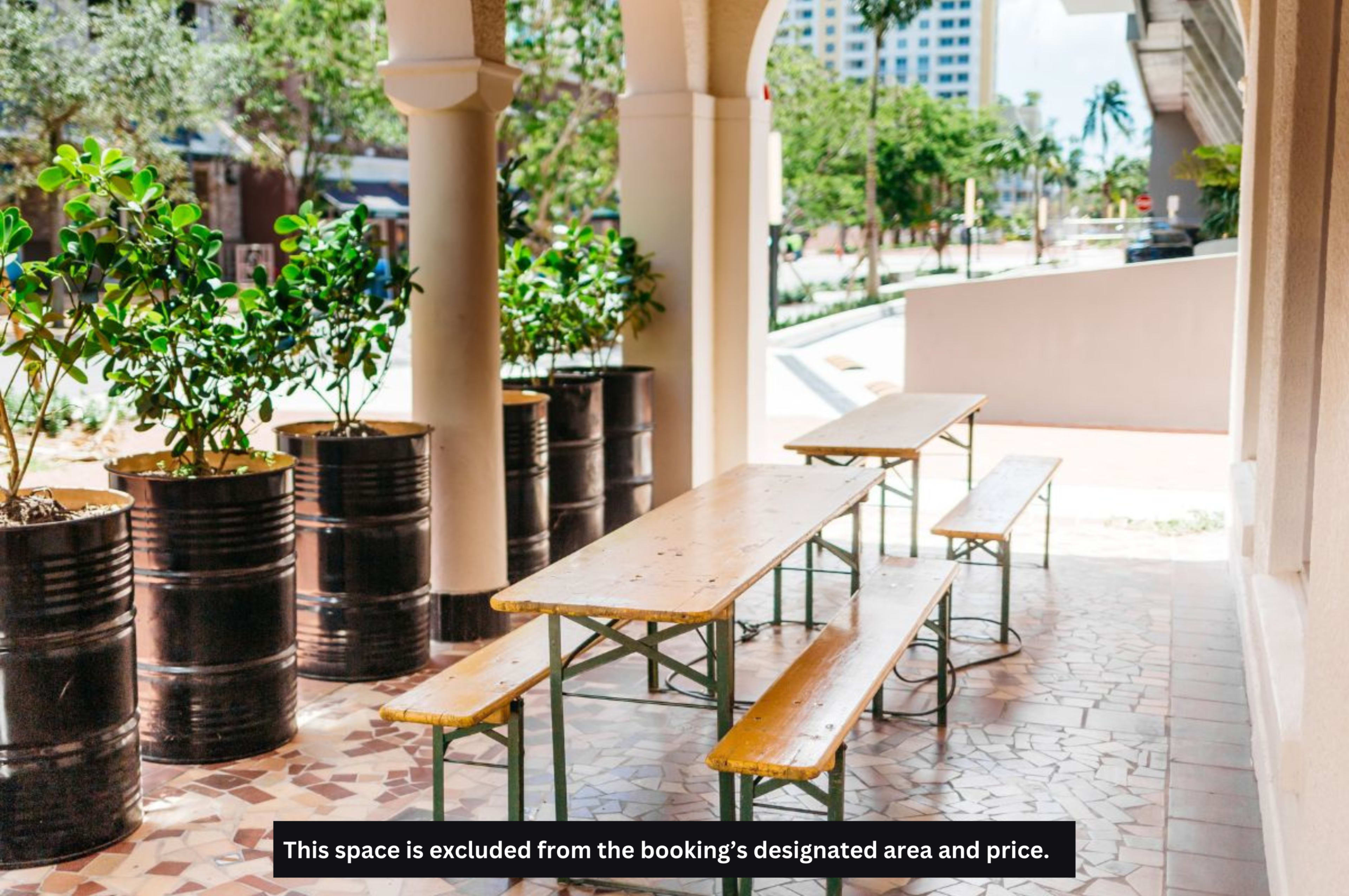 The image shows wooden picnic tables arranged on a tiled walkway beside potted plants and a view of a street.