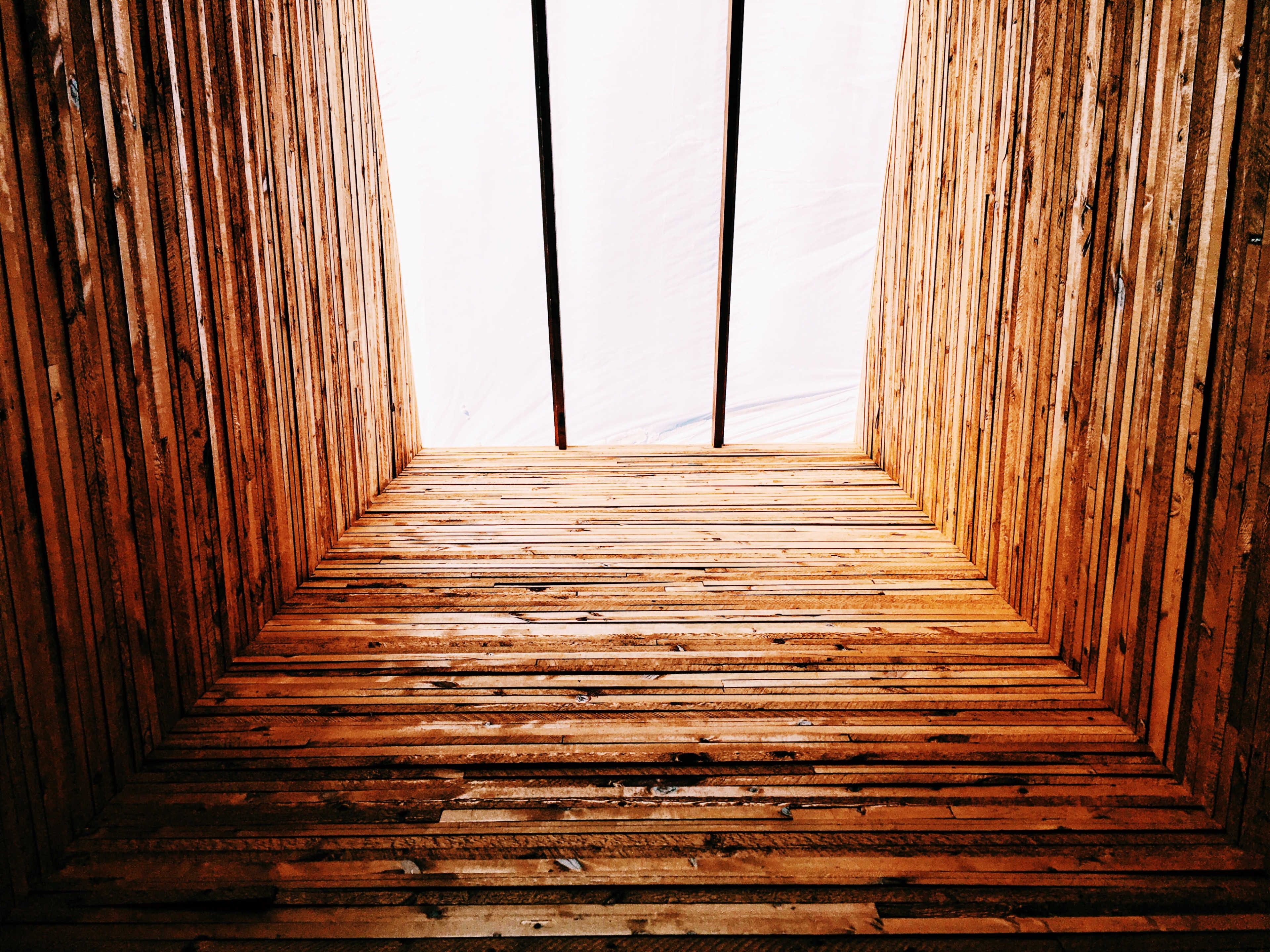 A view looking upward towards a light source through wooden beams arranged in a rectangular formation.