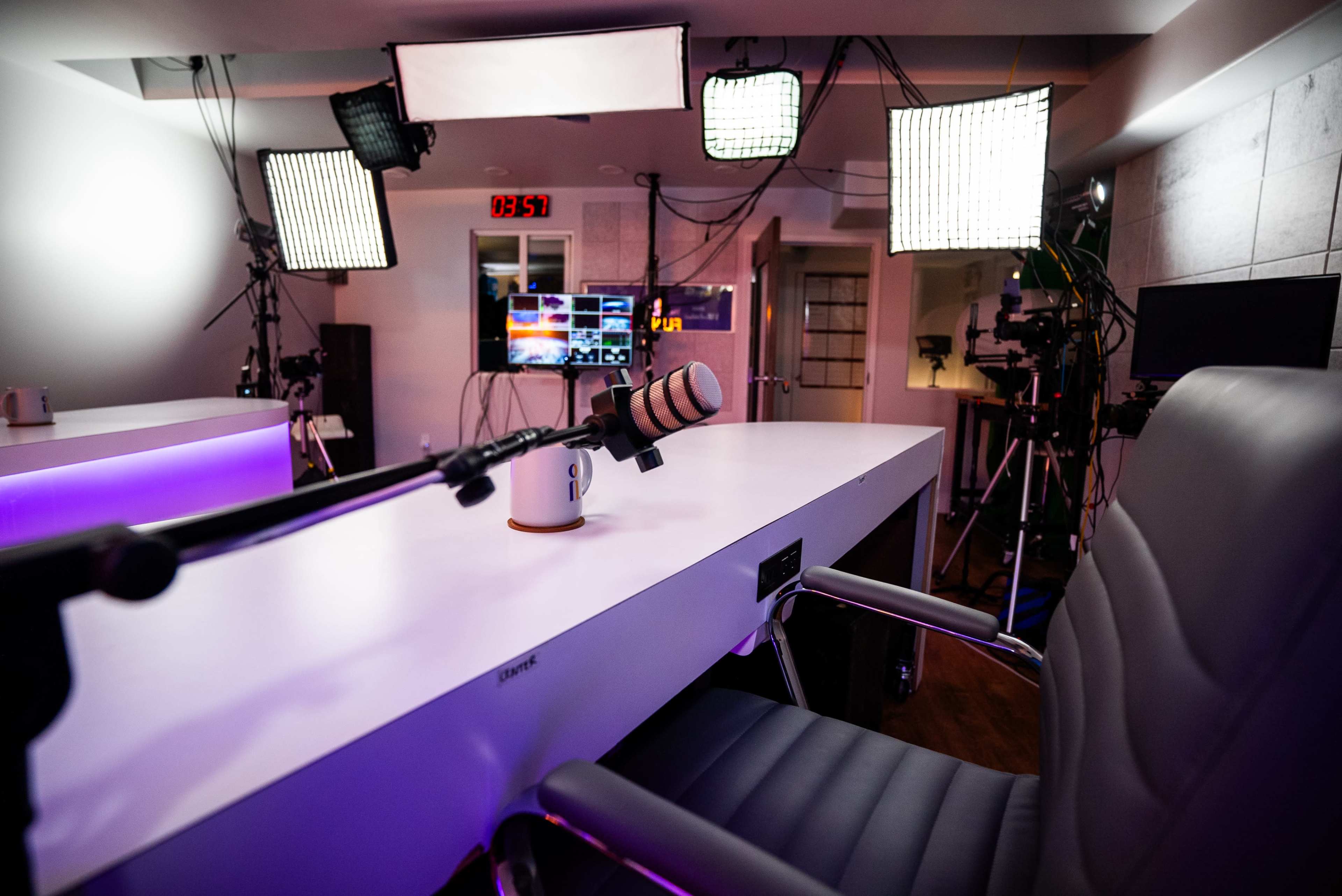 A recording studio setup features a large table with a microphone, an office chair, and multiple lights positioned around the space.