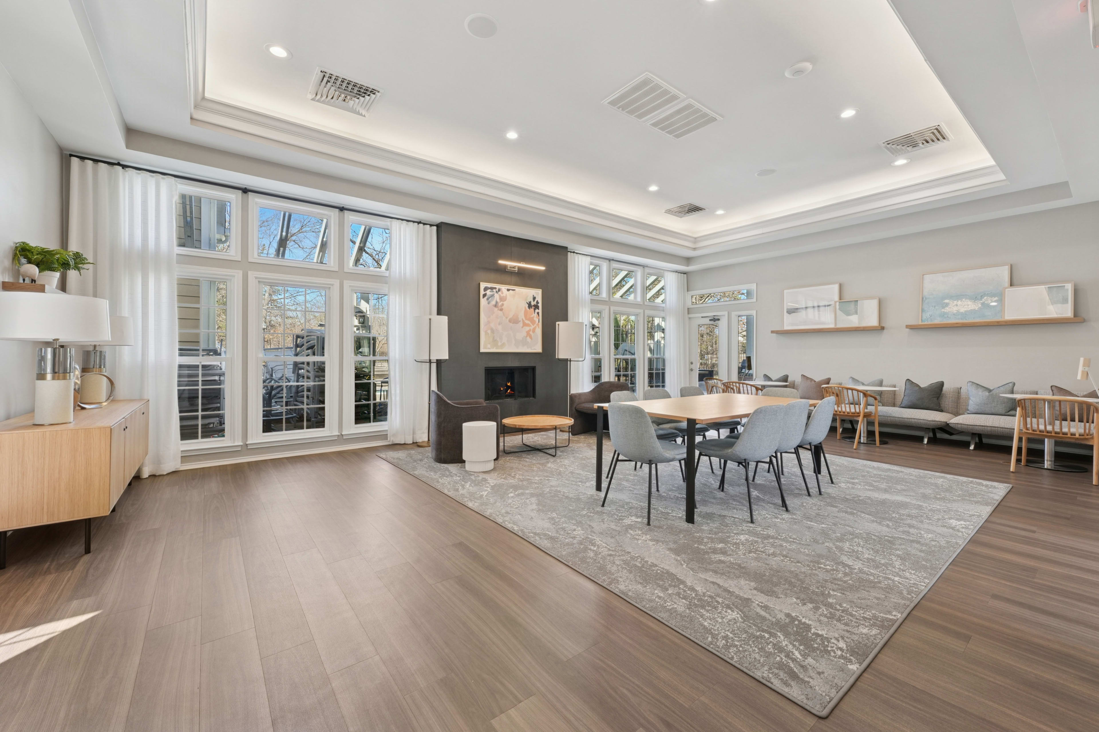 A spacious living area features large windows, a circular dining table surrounded by chairs, and a modern design with a light color palette.