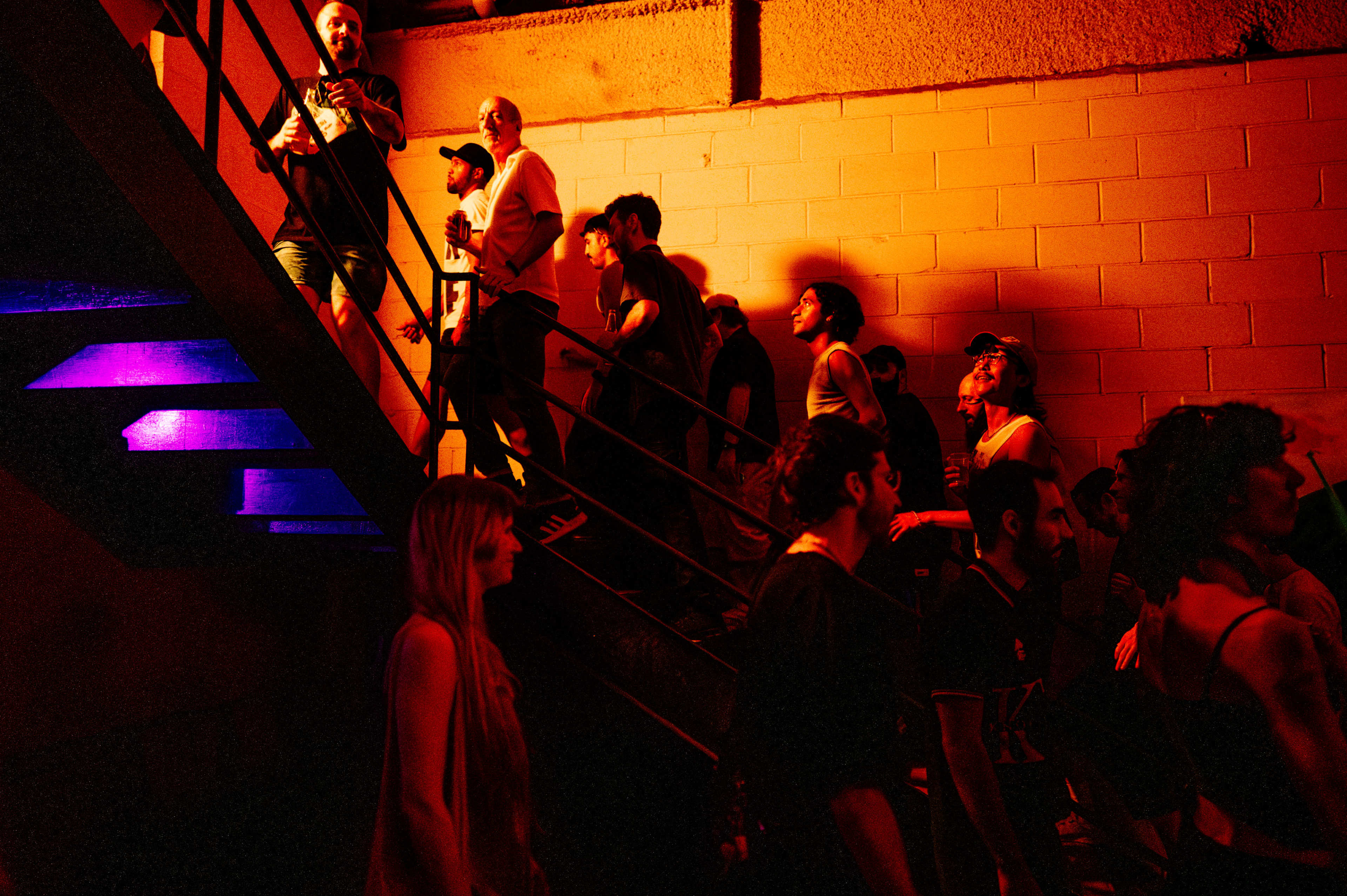 A group of people ascends a stairway, illuminated by colored lights, in a dimly lit setting.
