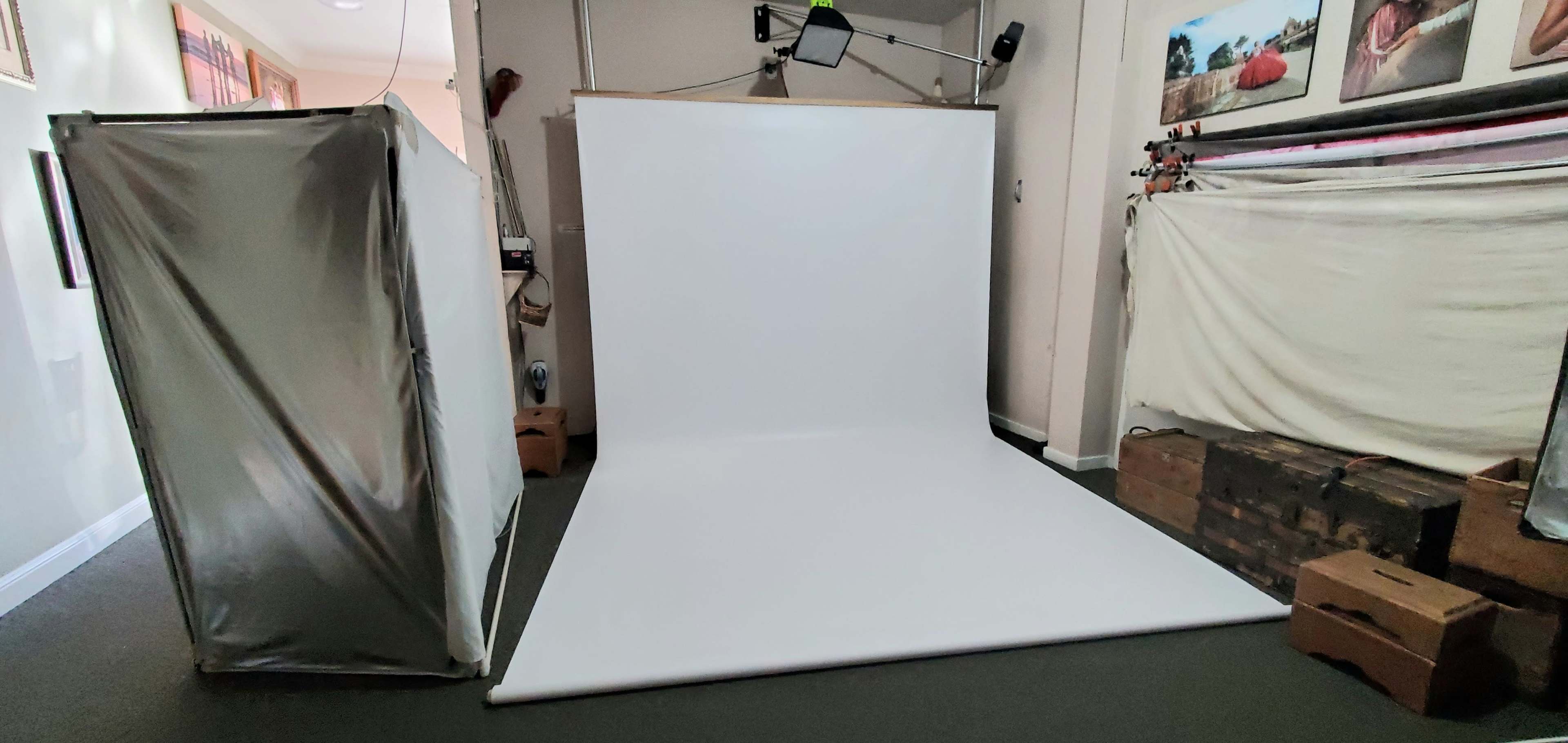 The image shows a photography studio with a white backdrop, softbox lighting, and various equipment arranged on the floor.