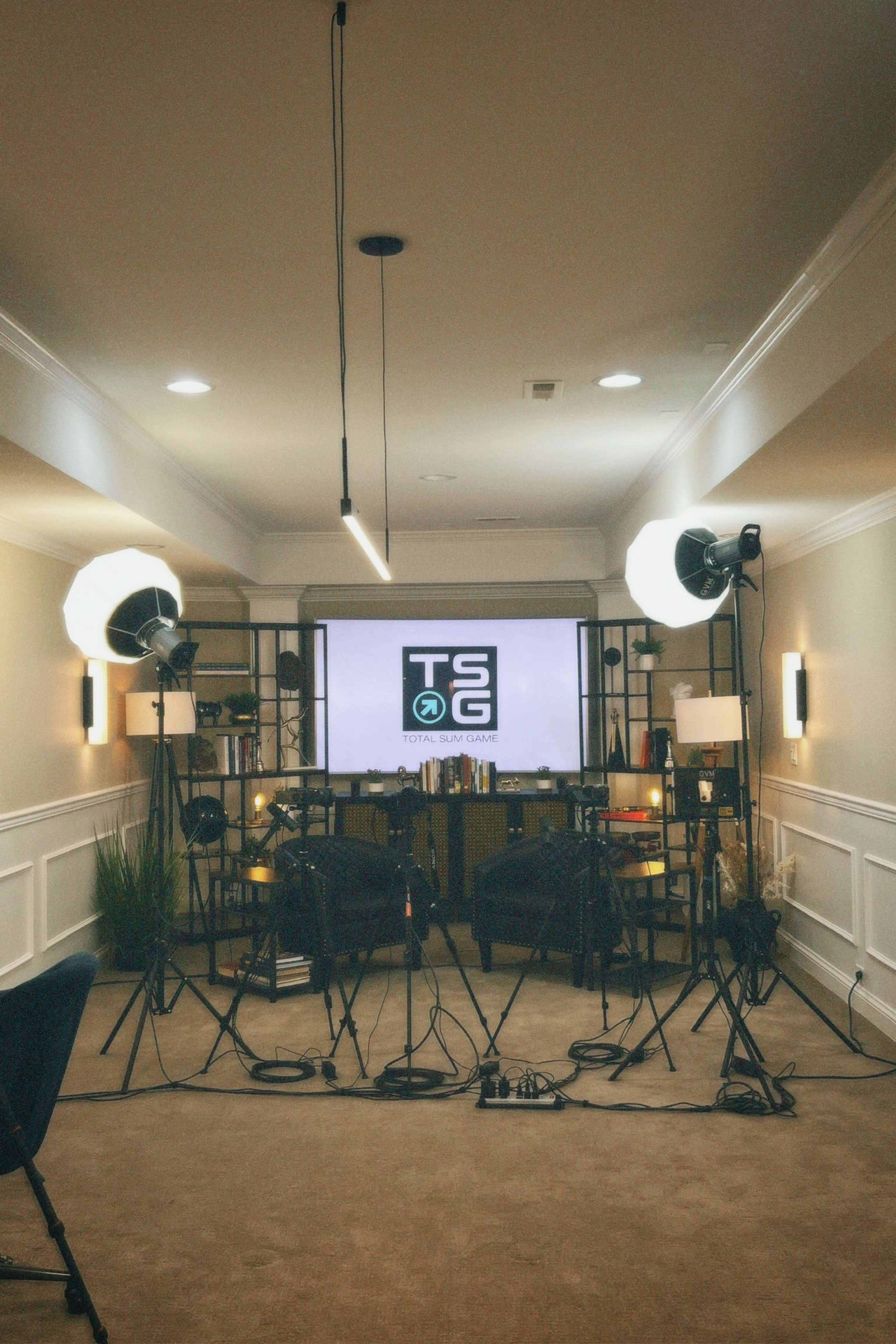 The image shows a studio setup with lighting equipment and a large screen displaying the logo of "TSG," set in a well-lit room.