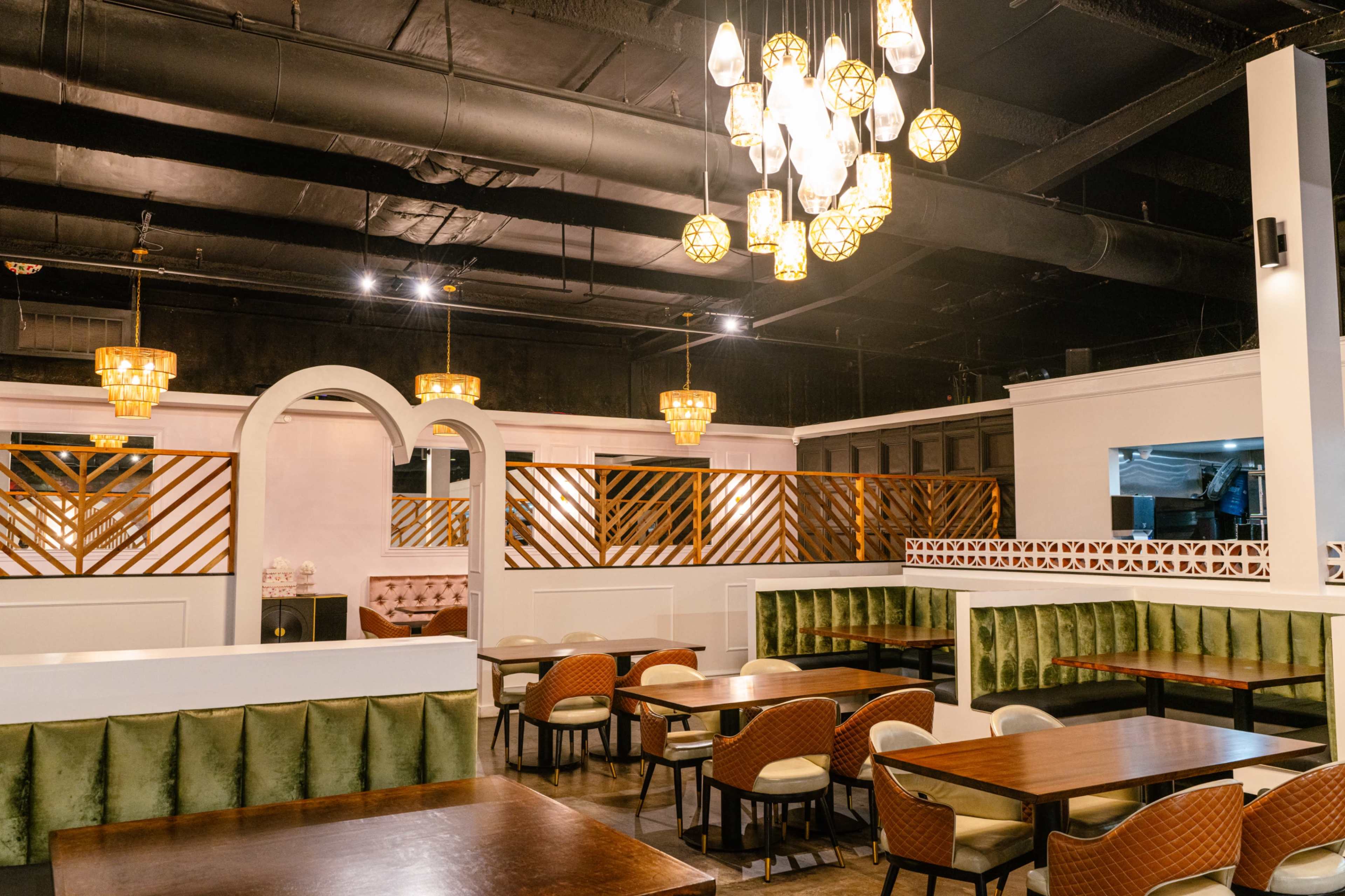The image shows a spacious restaurant interior featuring green upholstered seating, wooden tables, and decorative lighting.