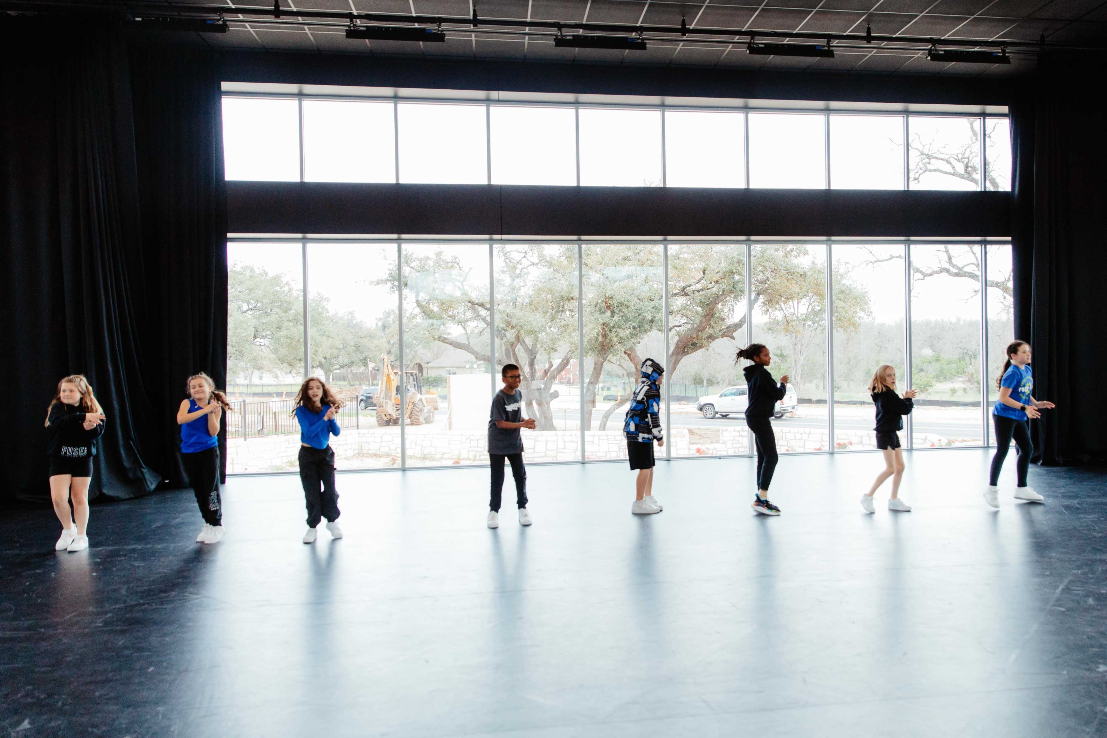 A group of children is dancing in a spacious studio with large windows.