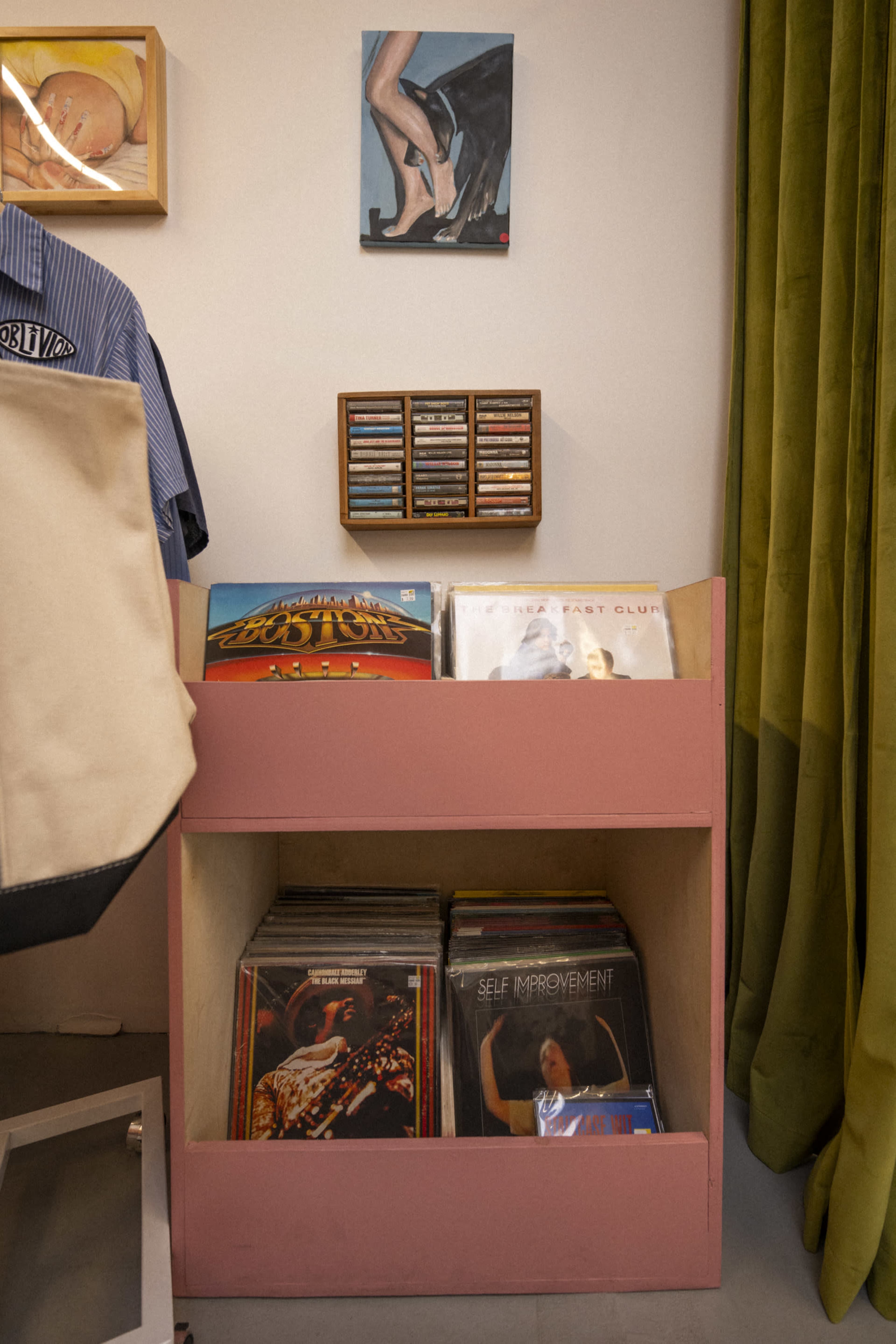 A wooden storage unit painted pink displays a collection of vinyl records alongside a small framed art piece on the wall above.