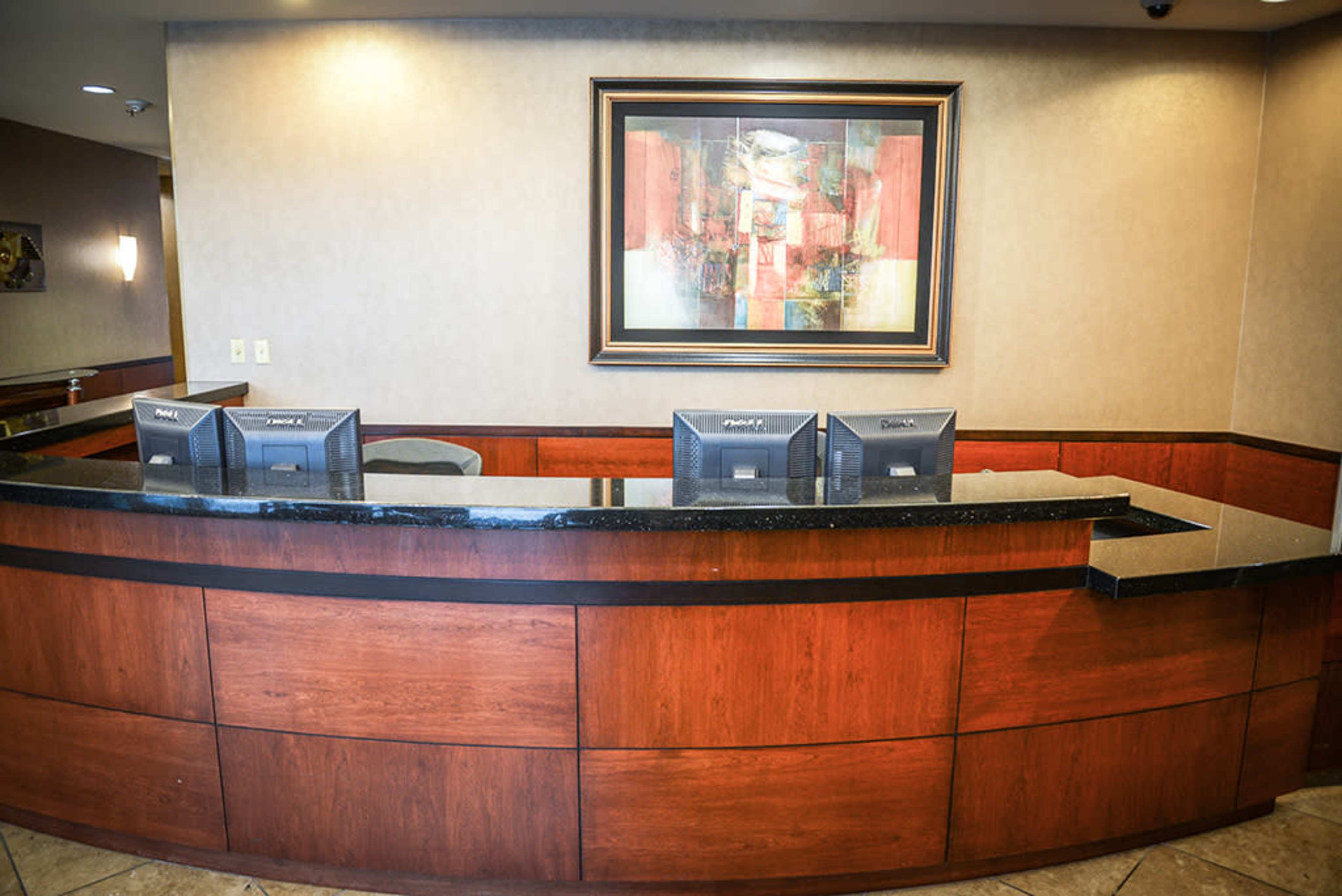 The image shows a reception desk made of dark wood and granite, featuring three computer monitors and a large abstract painting on the wall behind it.