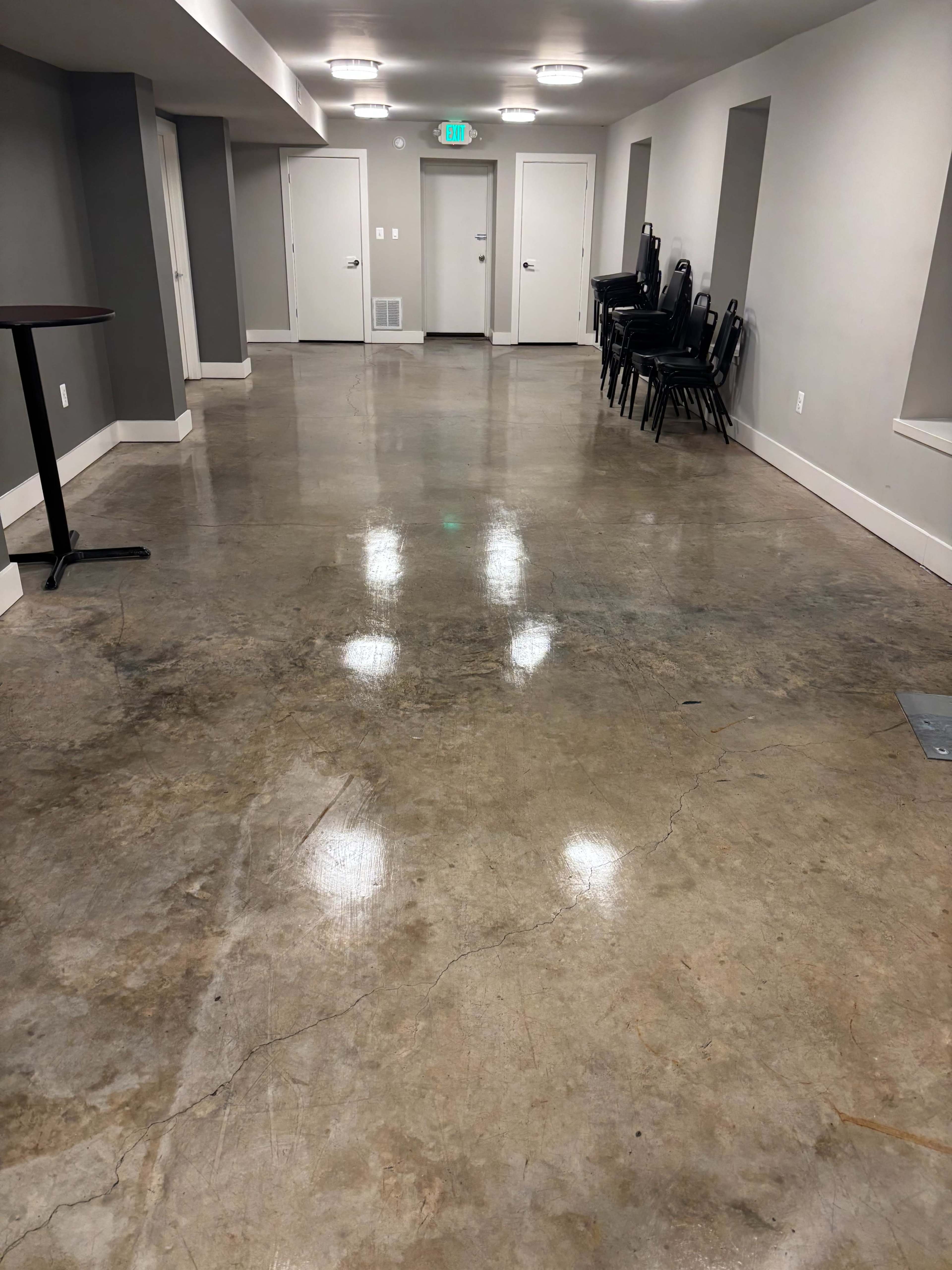 The image shows a wide hallway with polished concrete flooring and empty metal chairs stacked against the wall.