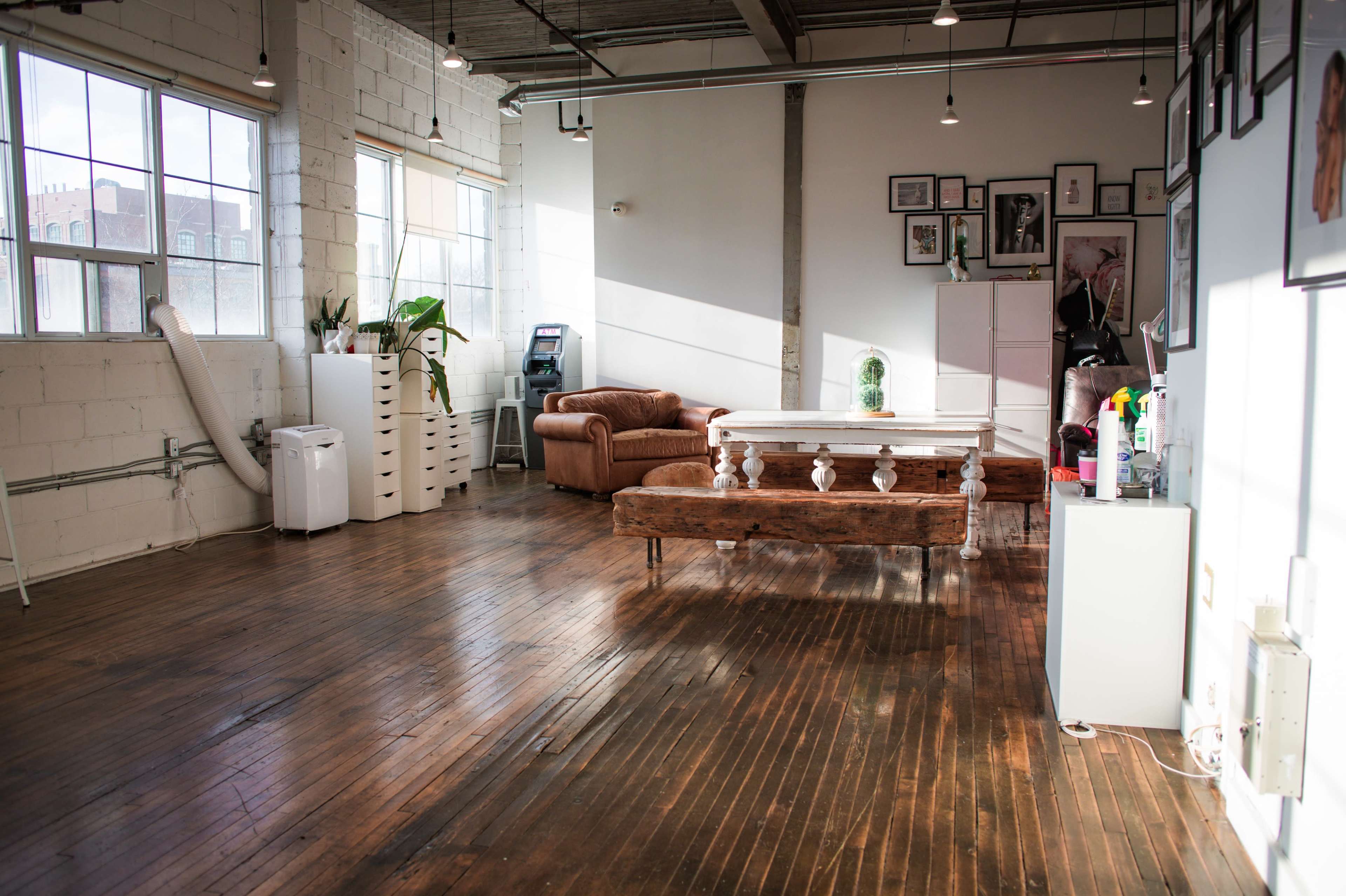 A spacious, brightly lit room with wooden floors, a large table, a brown couch, and various decor on the walls.