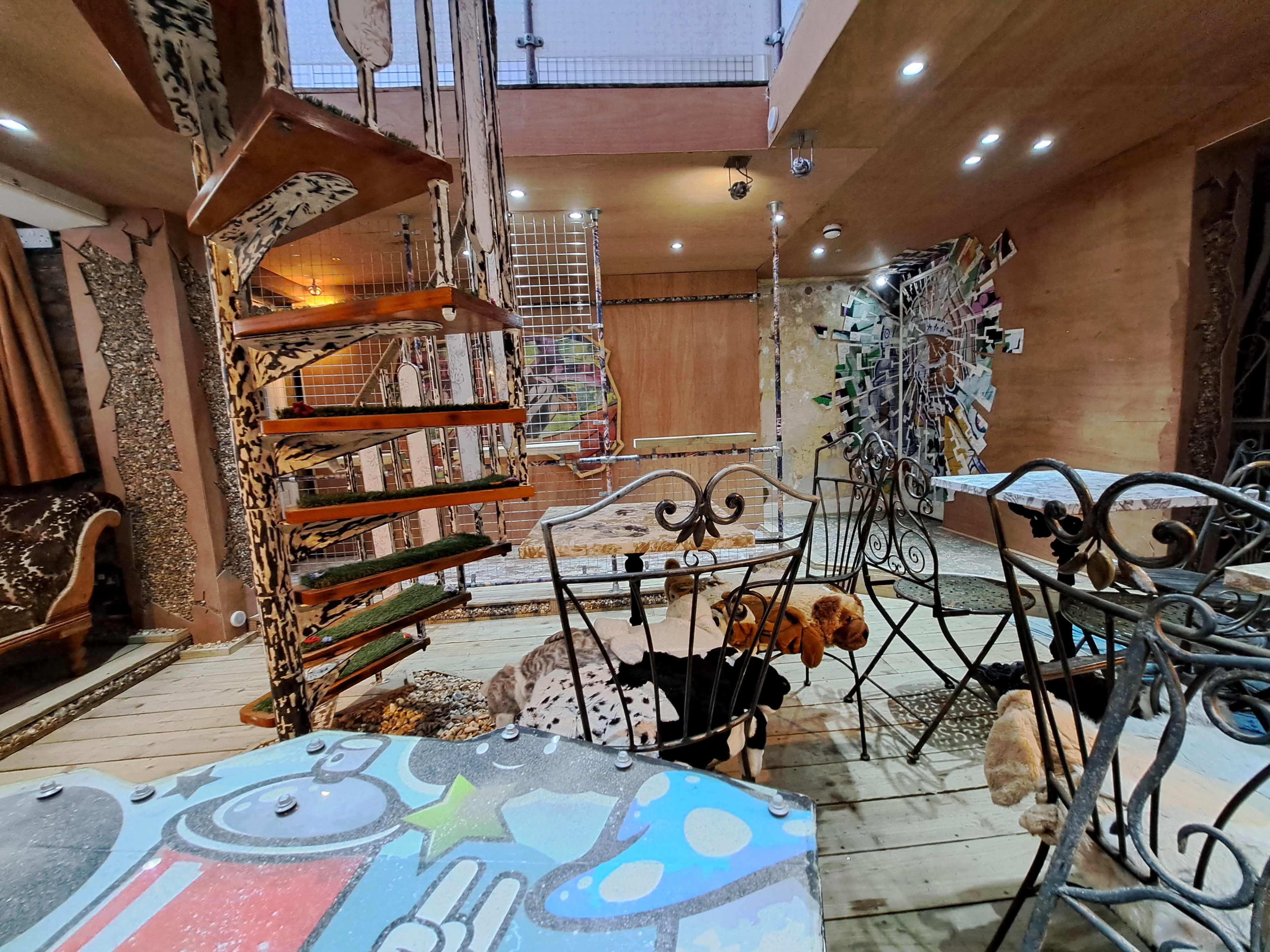 A multi-level art space featuring a spiral wooden staircase and eclectic decor including metal furniture and various artworks on the walls.