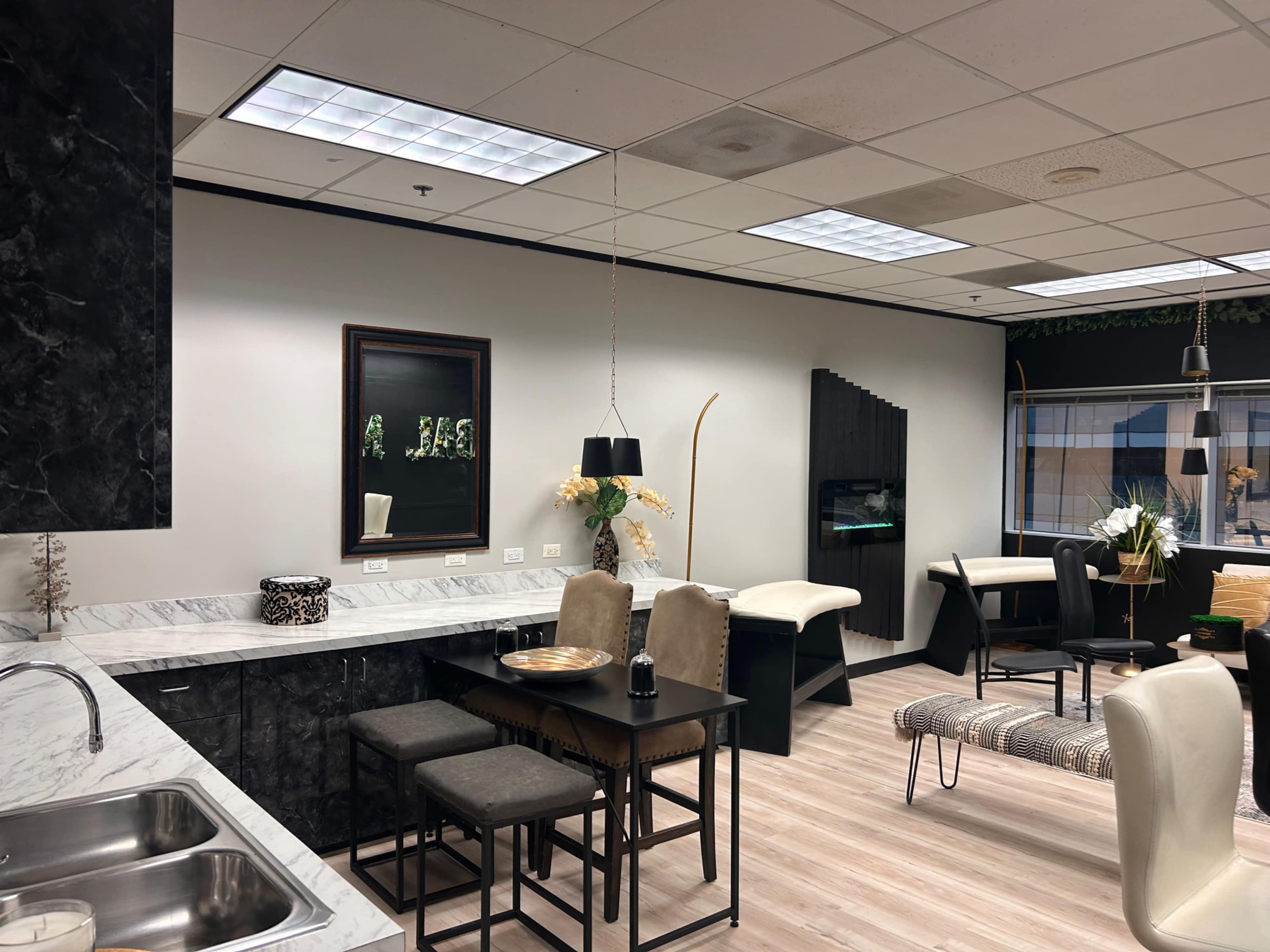 The image shows a modern kitchen area with a marble countertop, a dining set with stools, and a living space featuring a mix of furniture against a neutral-colored backdrop.