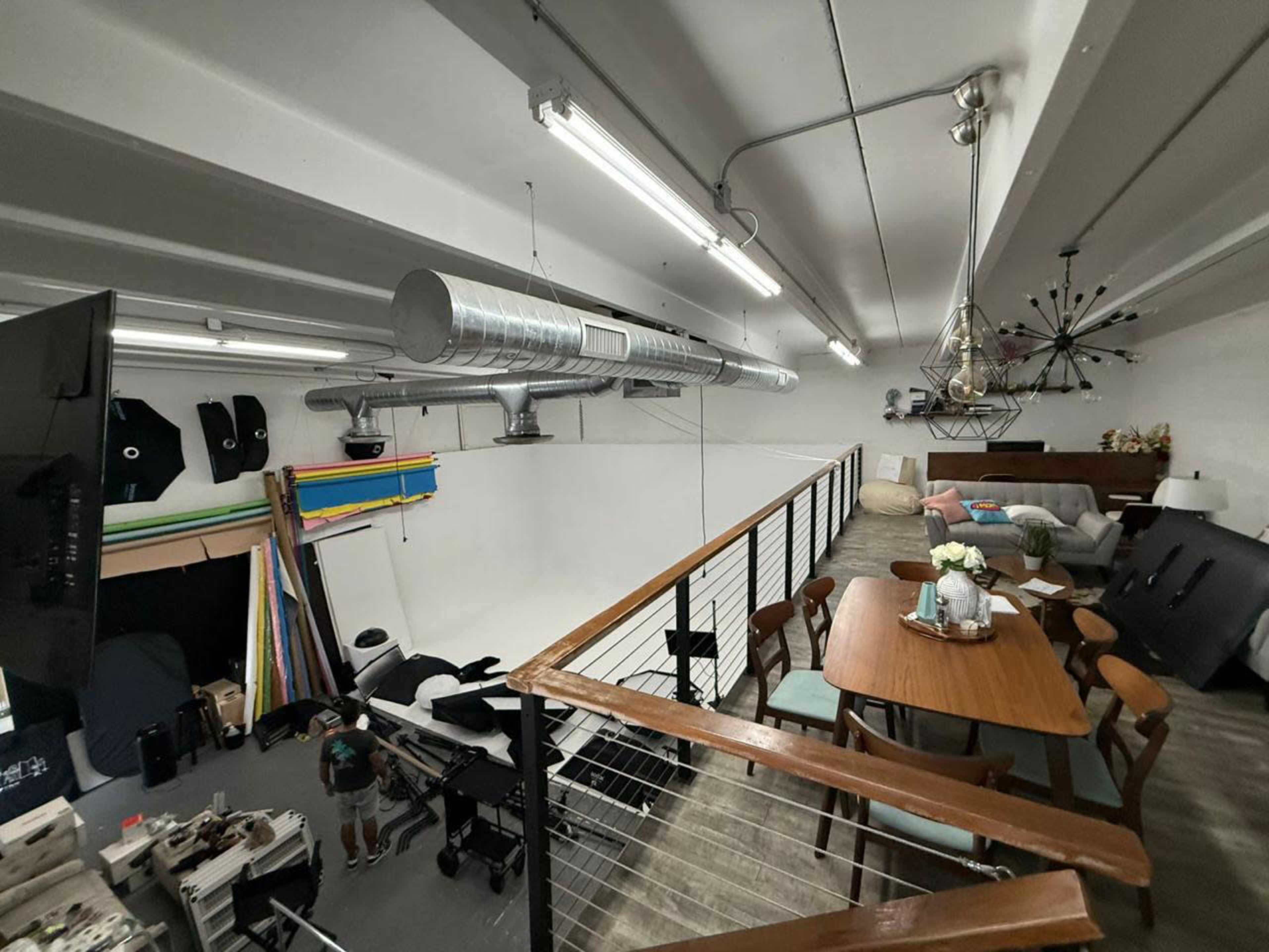 The image shows an interior space featuring a photography studio setup with various equipment, a dining table, and a lounge area.