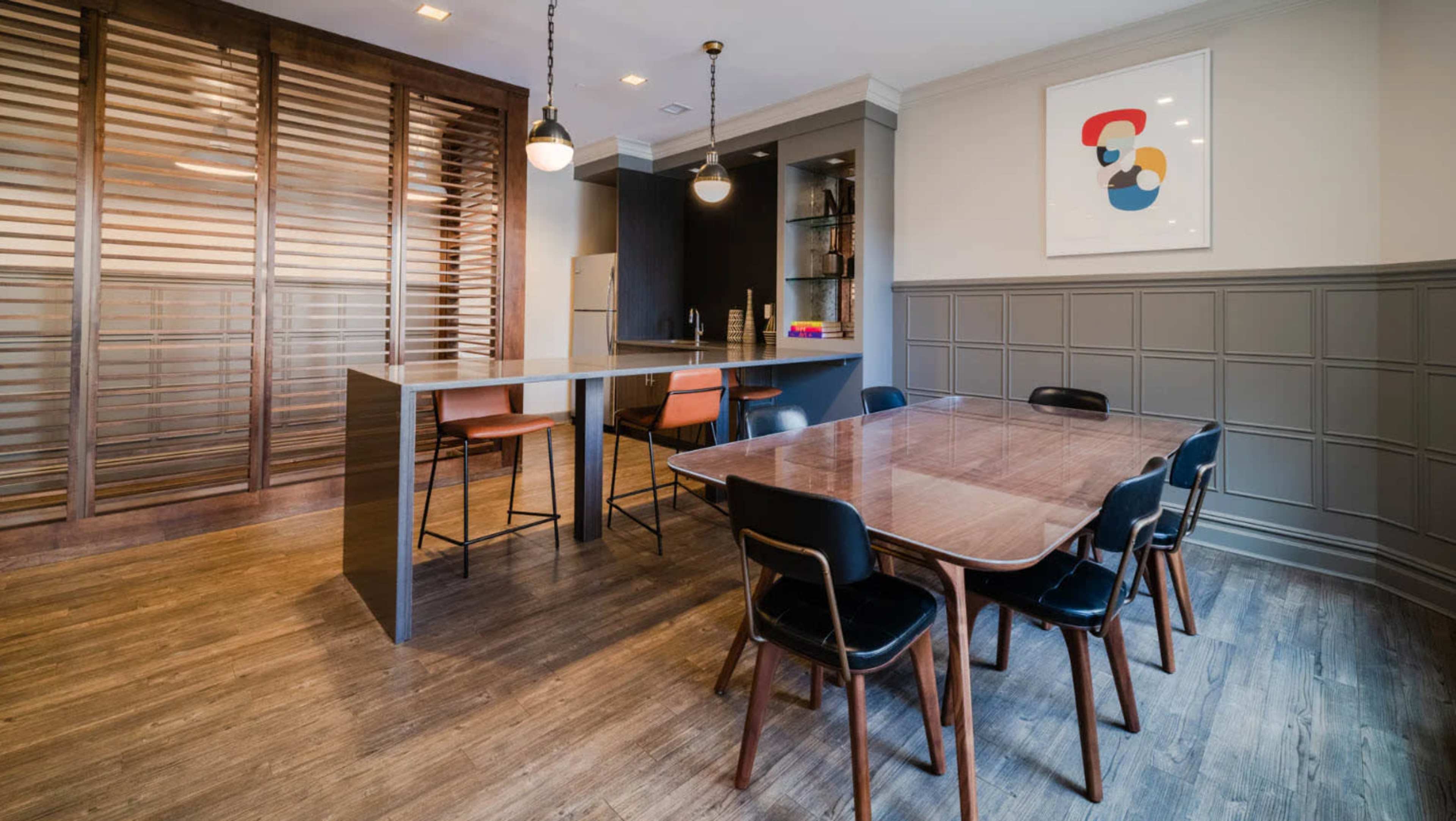 A modern dining area featuring a wooden table surrounded by black chairs, a kitchen bar with tall stools, and a wall with horizontal wooden slats.
