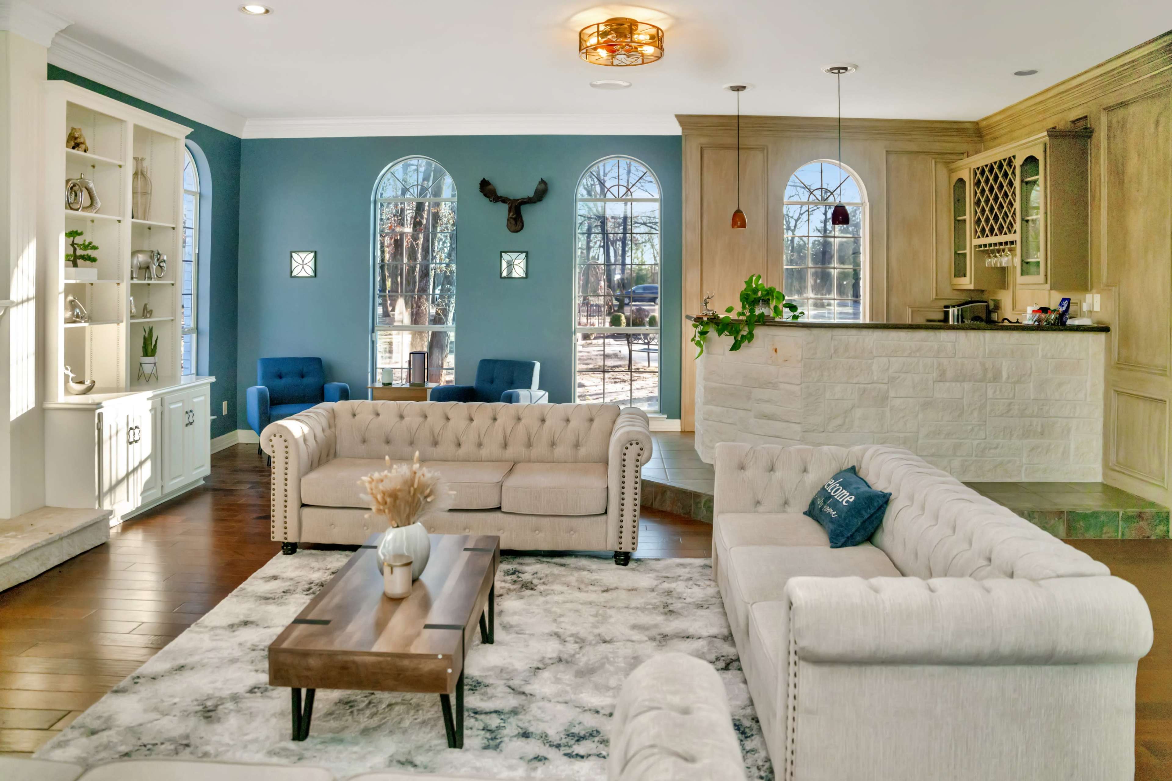 A spacious living room features two tufted sofas facing a wooden coffee table, with a stone fireplace and a bar area in the background.