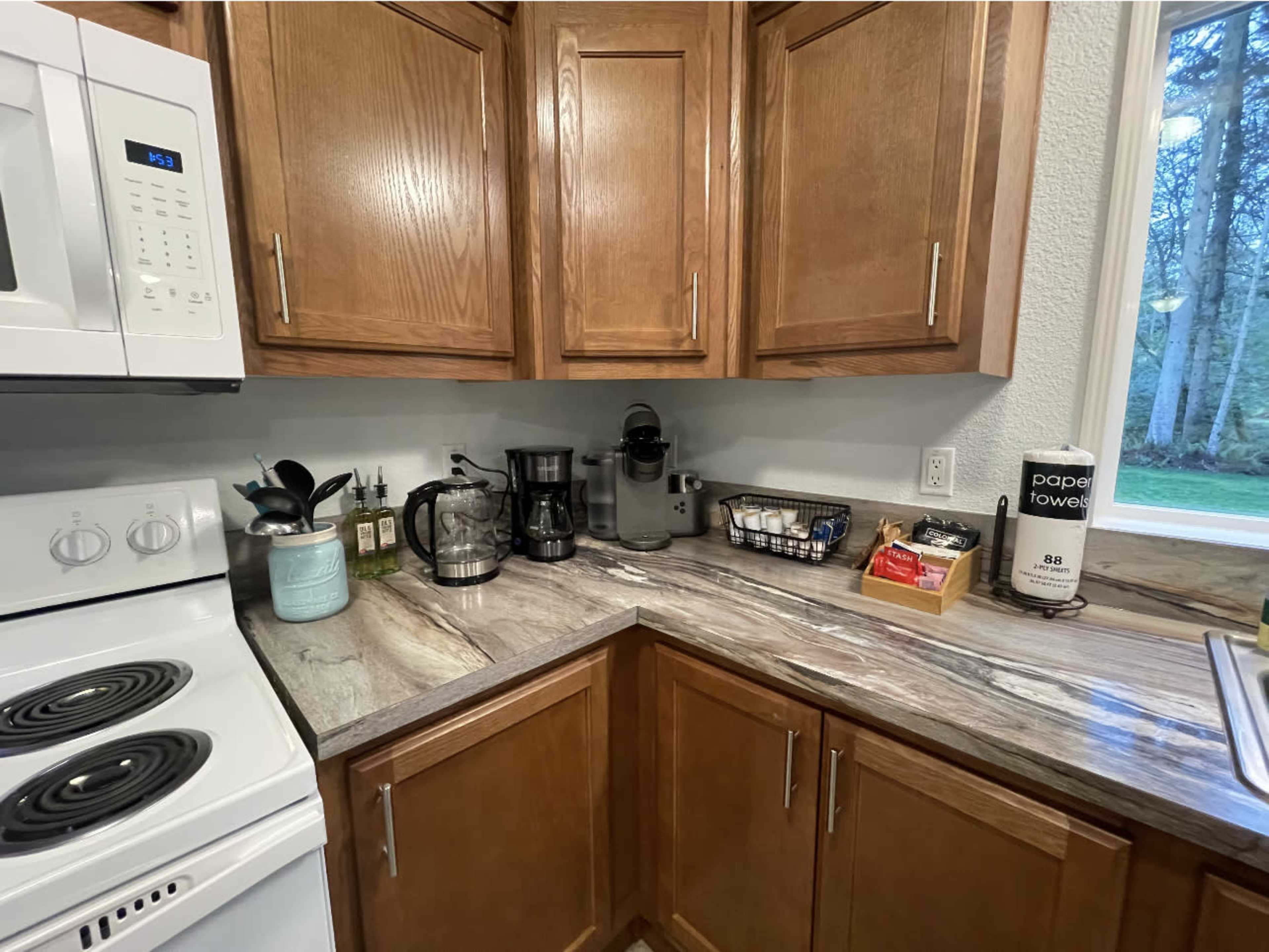 A kitchen corner features wooden cabinets, a white stove, a coffee maker, a blender, and various kitchen supplies arranged on a countertop.