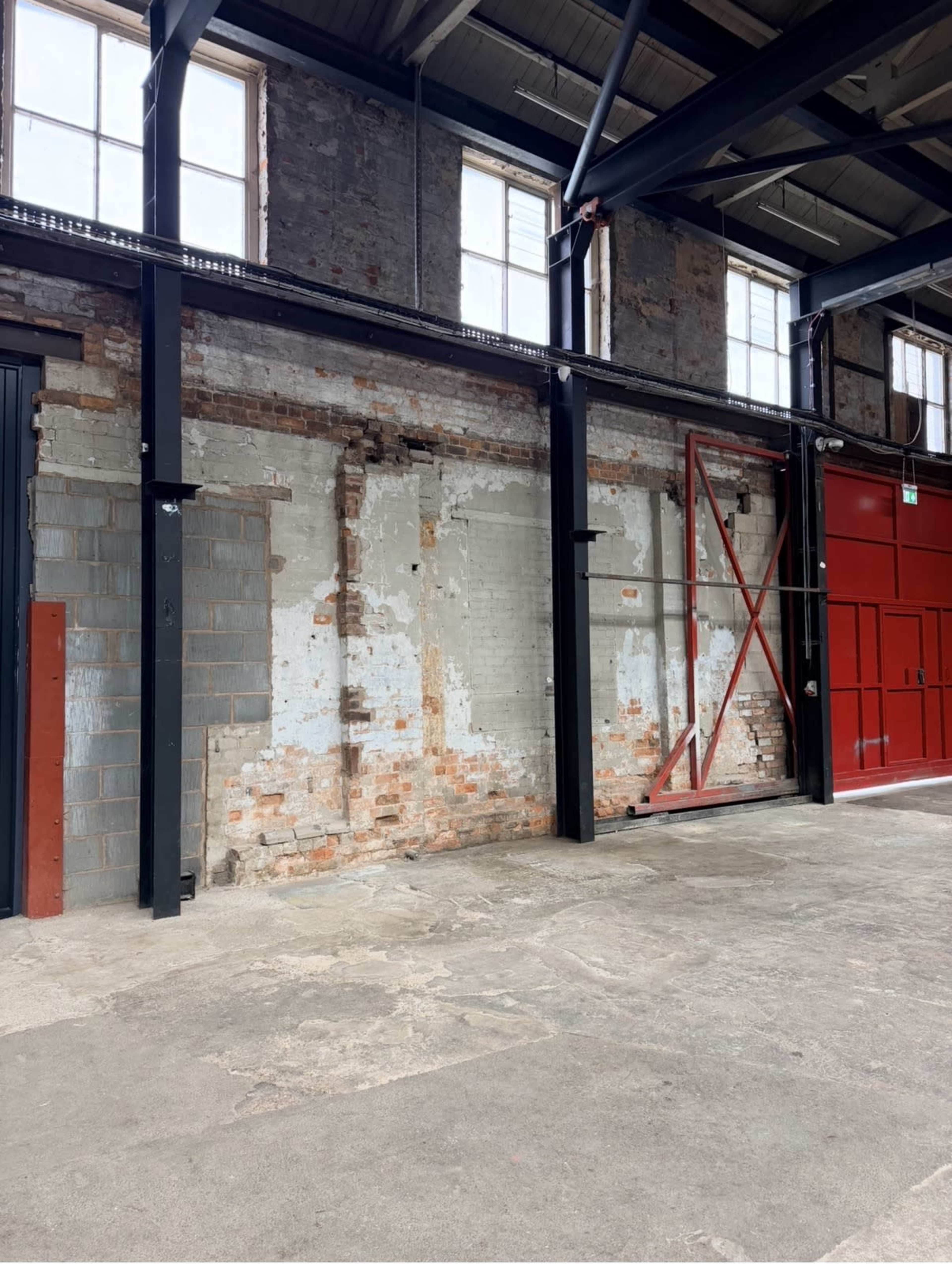 The image shows an industrial interior with exposed brick walls and metal beams, featuring a section of red-painted doors.