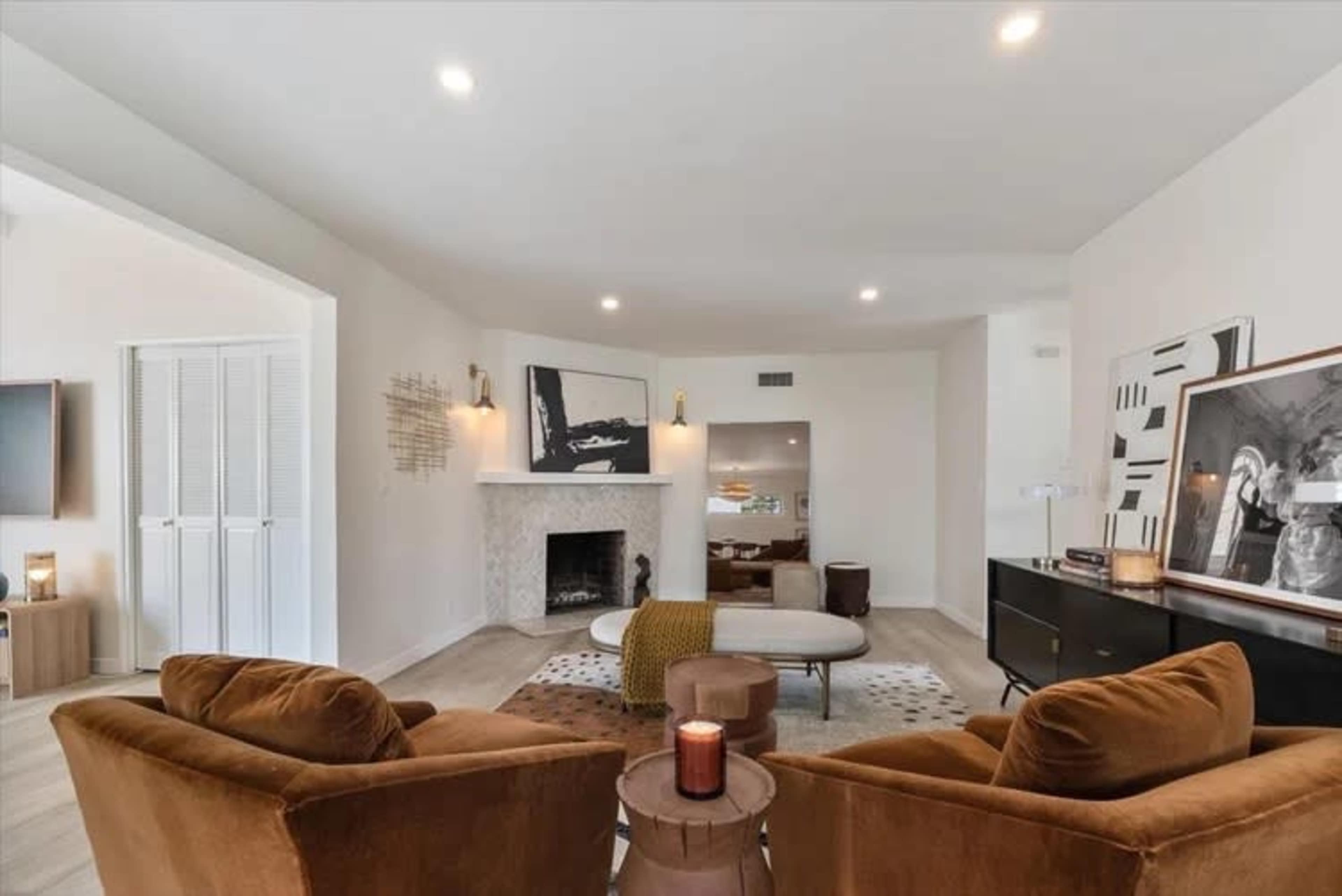 The image shows a modern living room featuring two brown armchairs, a round coffee table, a fireplace, and decorative artwork on the walls.