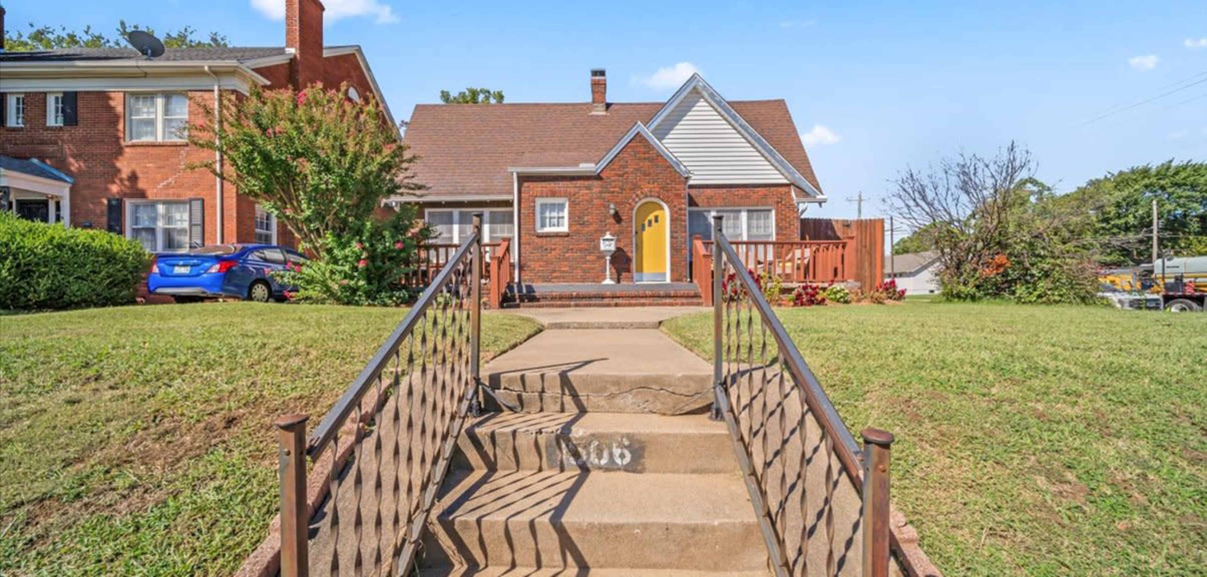The image shows a brick house with a gabled roof, a front porch, and a set of stairs leading to the entrance.