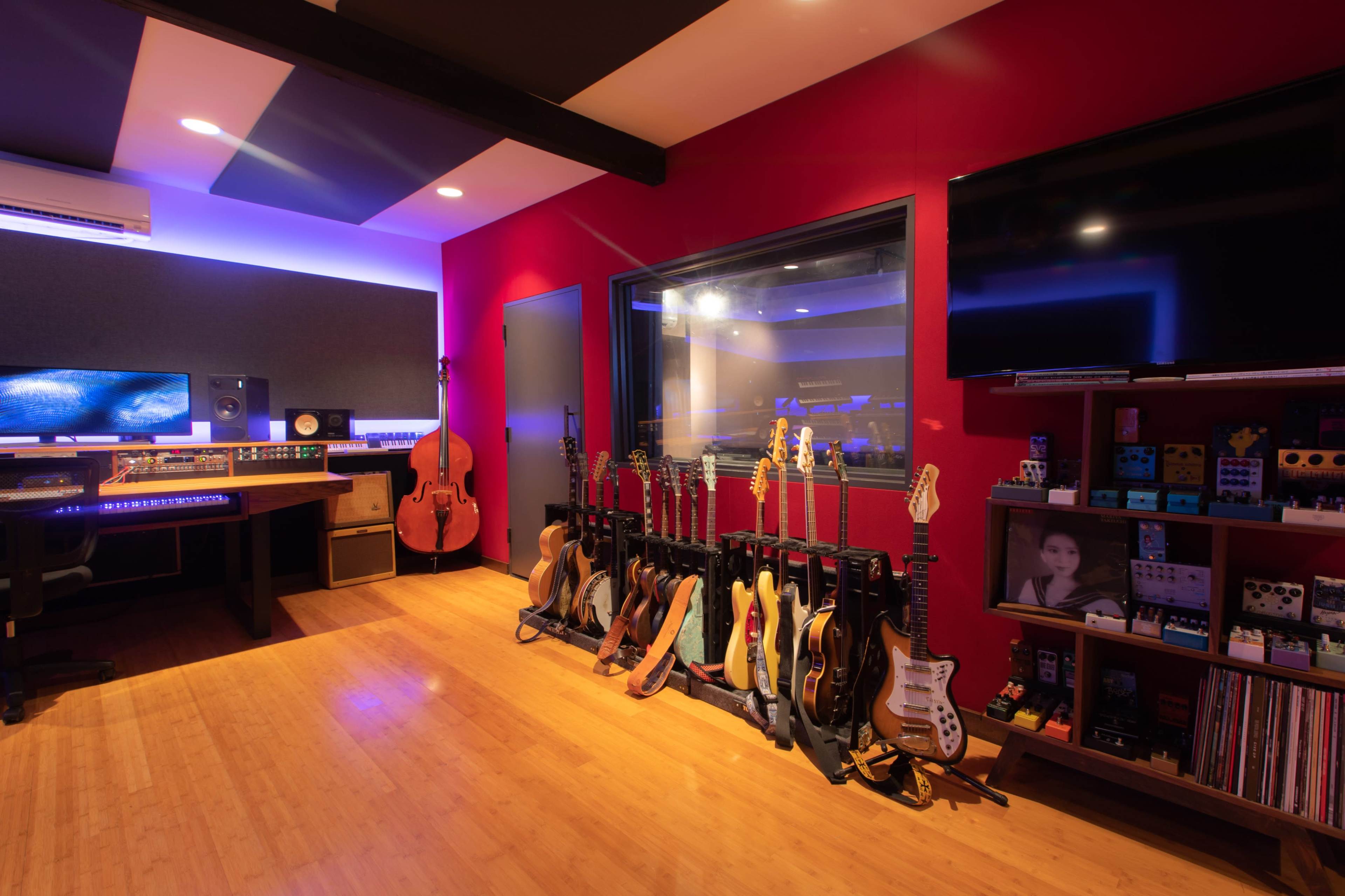 A music studio features a control desk, various guitars on a rack, and a wall of sound equipment under ambient lighting.