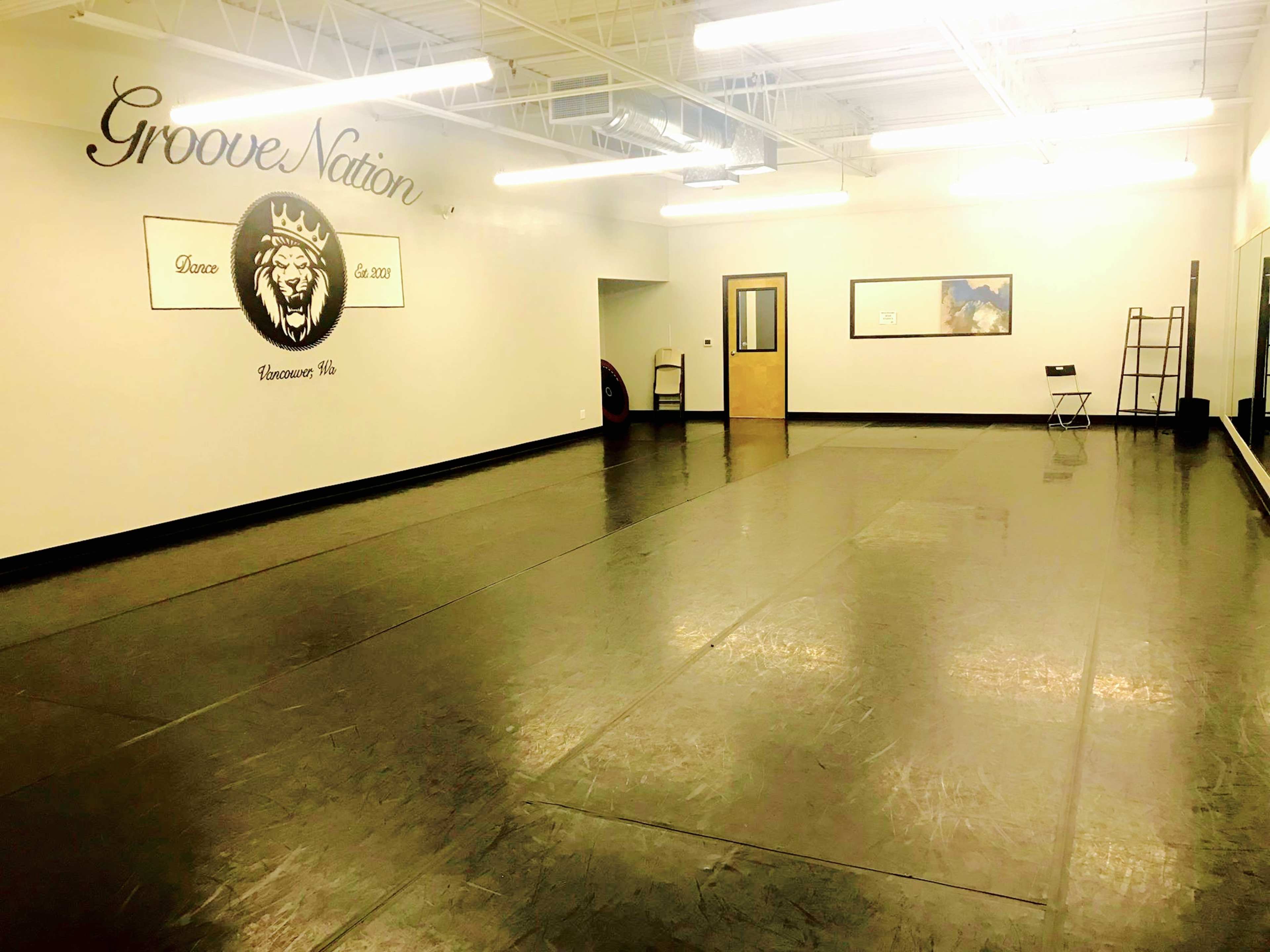 A spacious dance studio with a black floor, mirrored walls, and a logo featuring a lion, labeled "Groove Nation," is shown.
