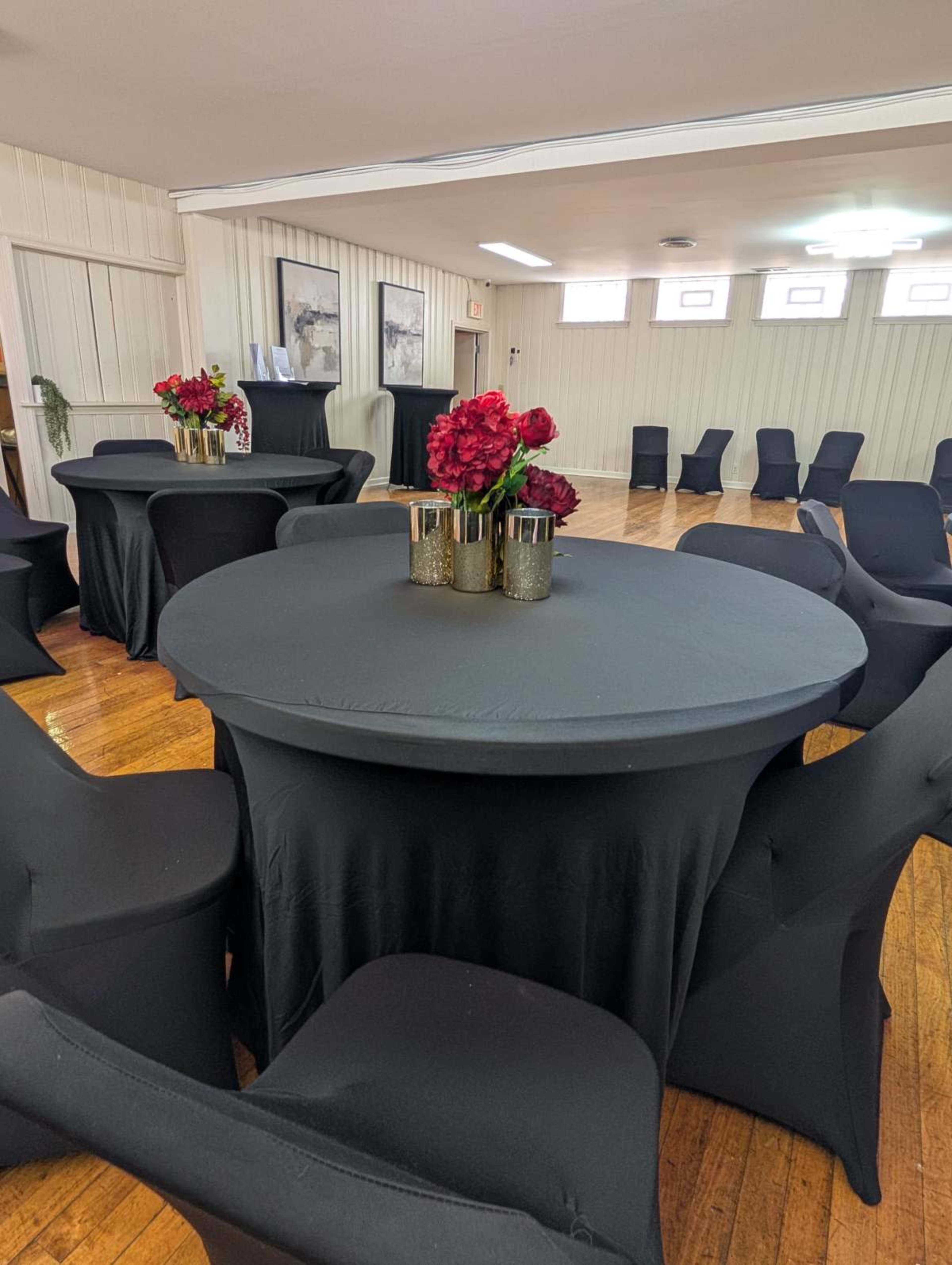 The image shows a neatly arranged venue with round tables covered in black tablecloths and elegant floral centerpieces surrounded by black chairs.