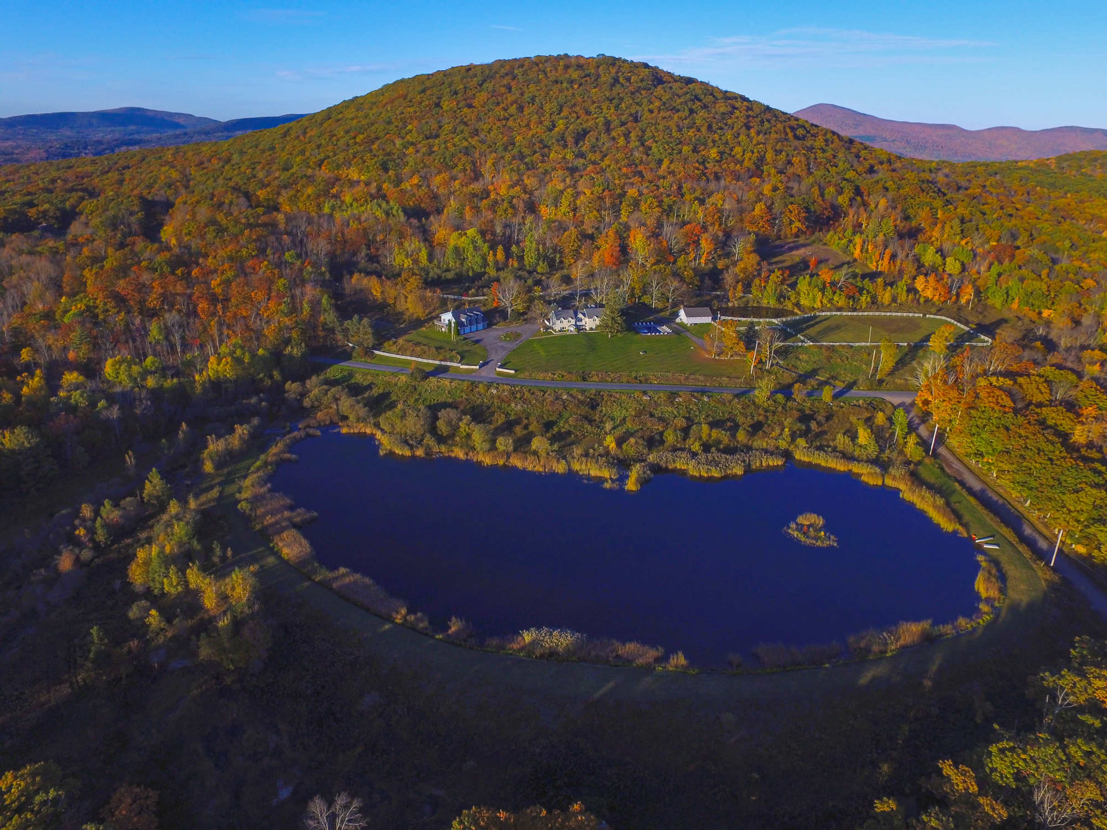 Aerial view of a pond surrounded by autumn foliage and a hill in the background.