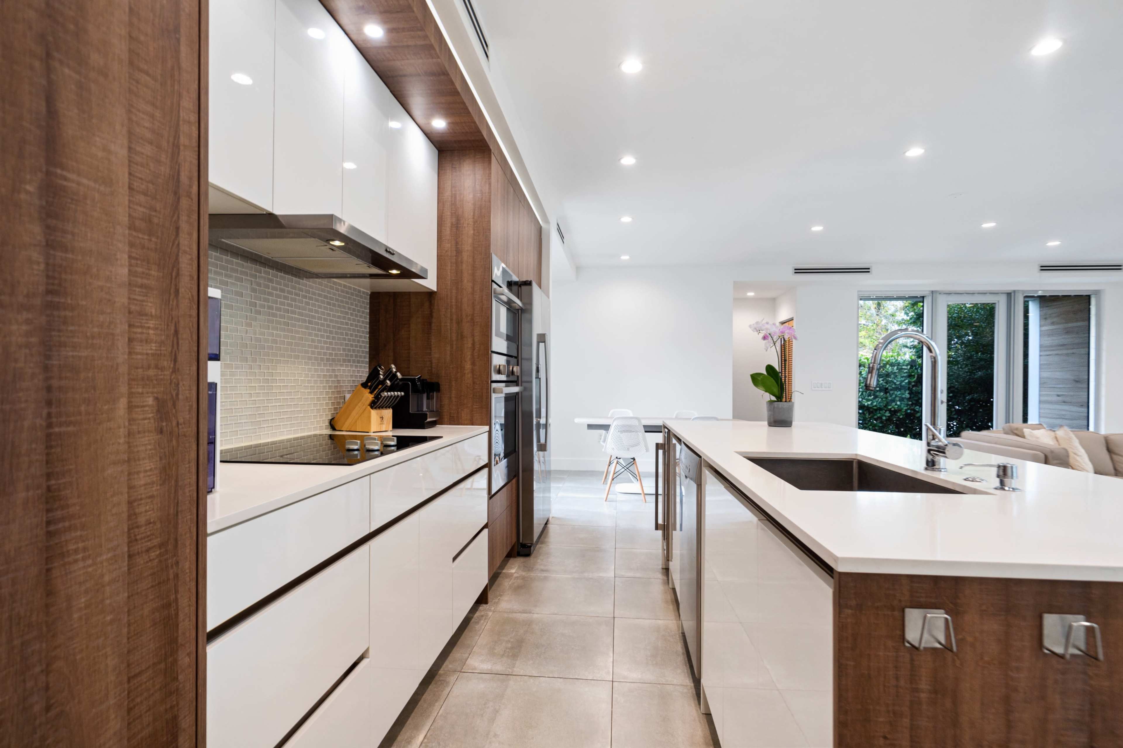 A modern kitchen featuring a mix of wooden and white cabinetry, stainless steel appliances, and a central island with a sink.