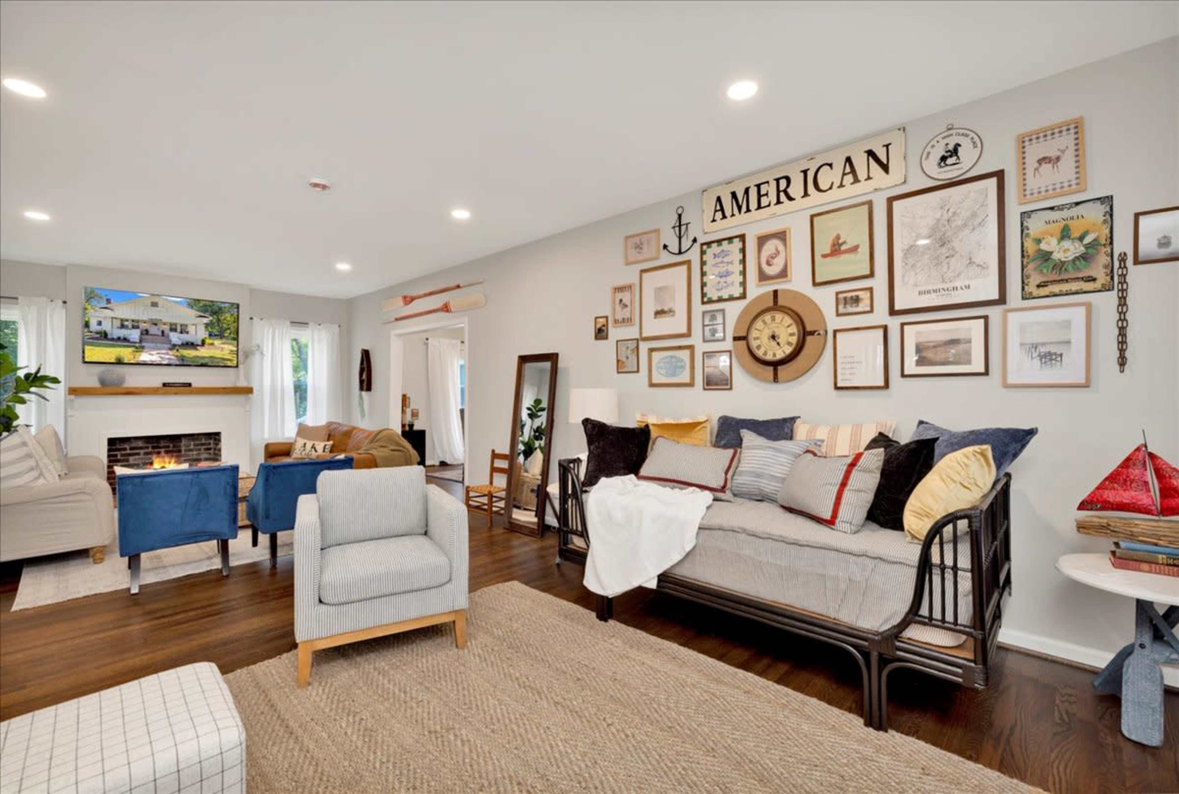 The living room features a seating area with a daybed, a cozy sofa, and a TV mounted above a fireplace, all adorned with a gallery wall of framed artwork and decorative items.