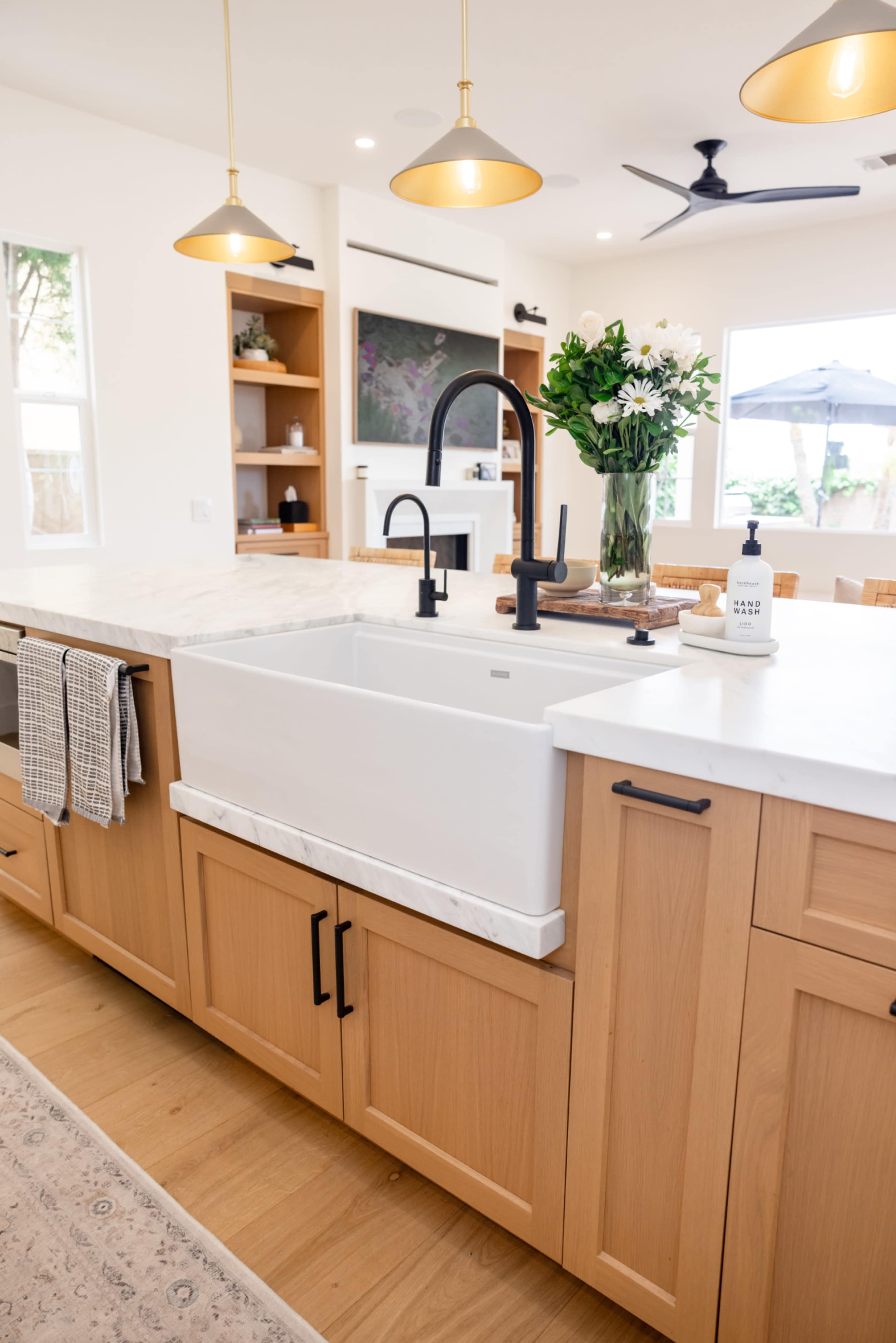 The image shows a modern kitchen with a farmhouse sink, wooden cabinetry, a marble countertop, and pendant lighting.