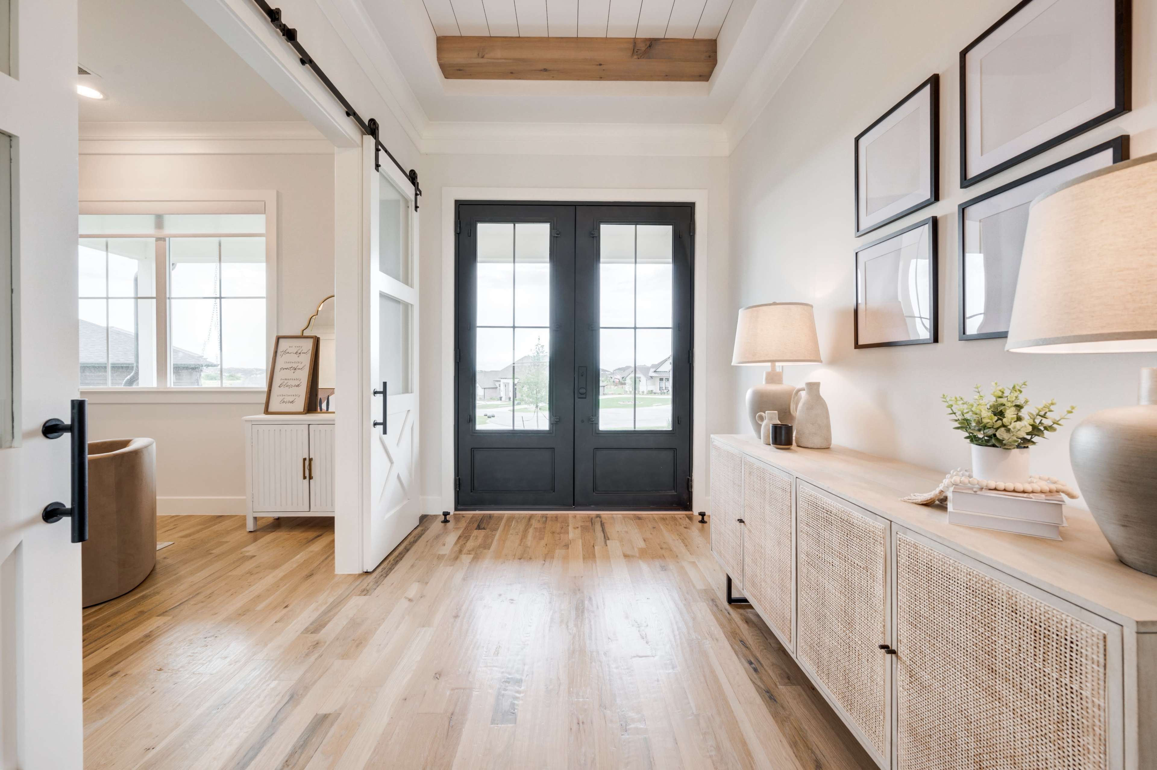 An entryway featuring double doors, a console table with decorative items, and framed pictures on the wall.