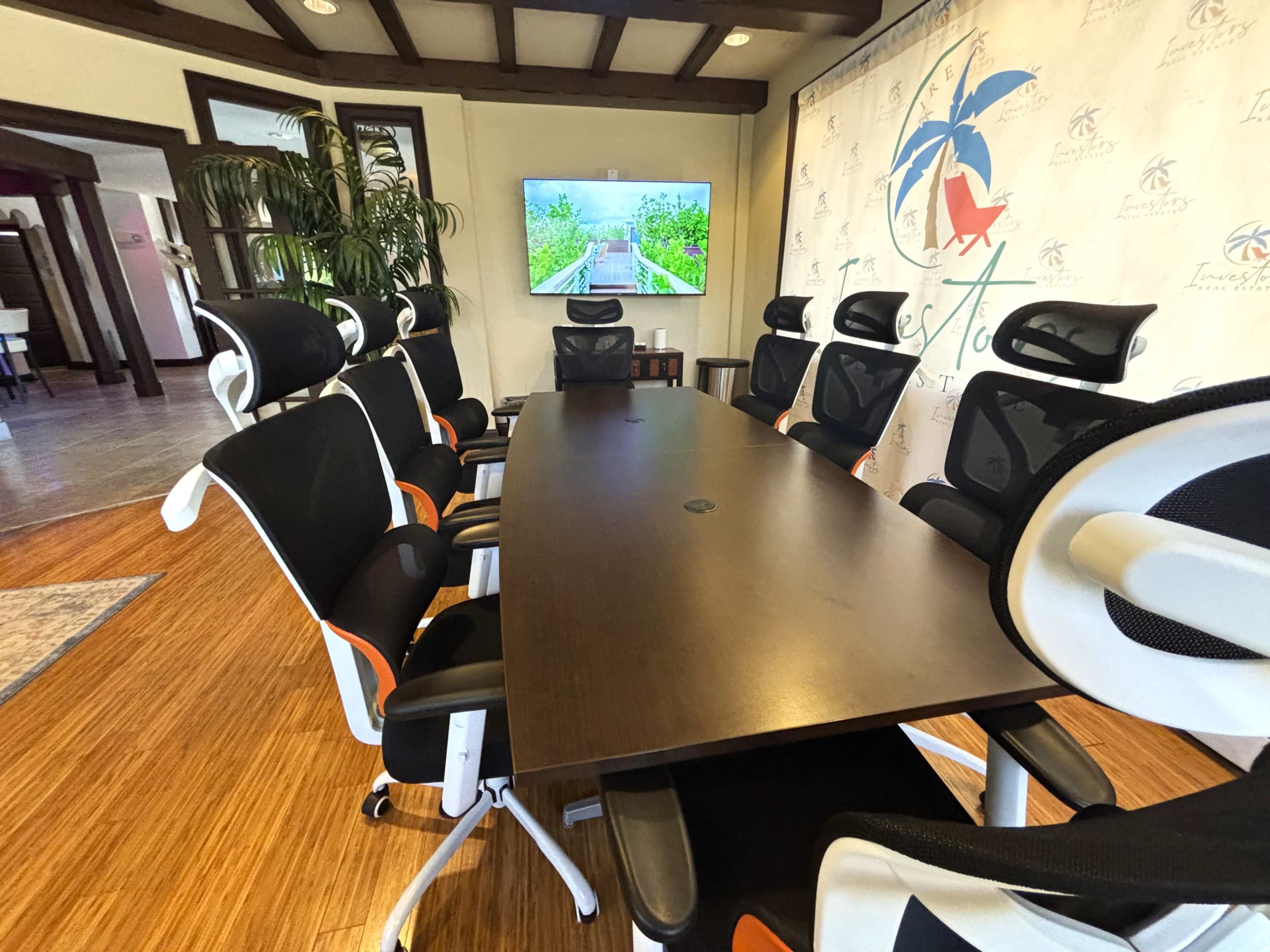 A modern conference room features a long table surrounded by ergonomic chairs, with a large screen displaying a serene landscape in the background.