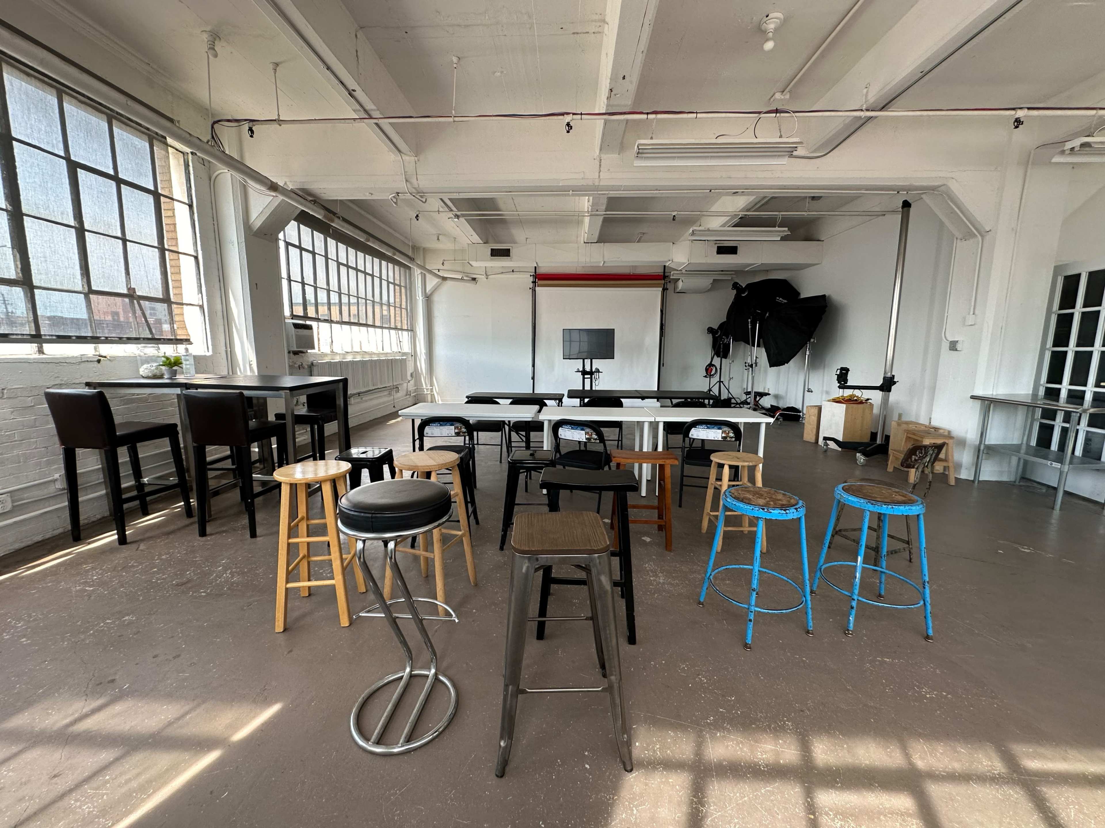 The image shows an empty studio space with various types of stools and tables arranged in a well-lit, open area.