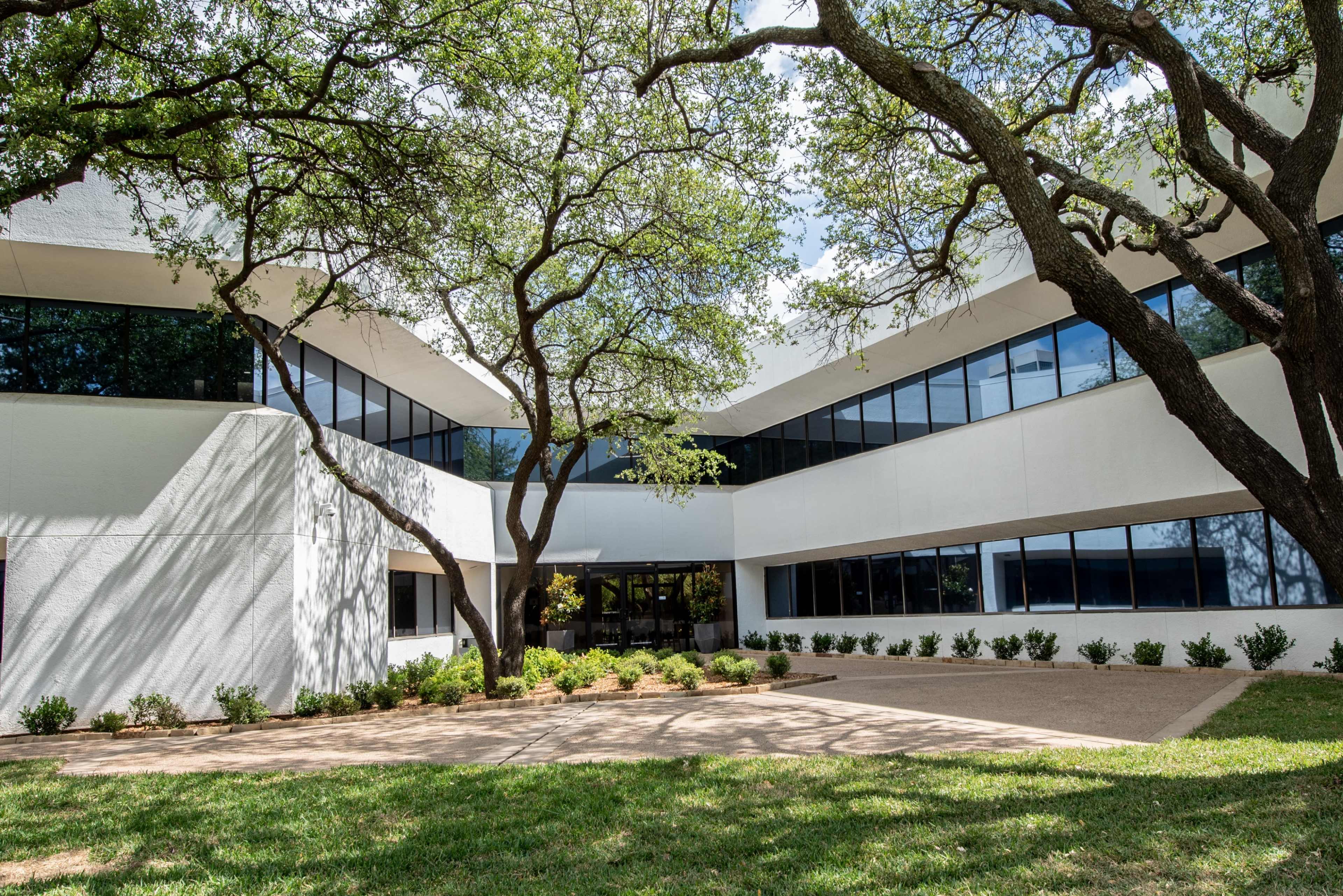 A modern building with angular architecture is surrounded by trees and a landscaped area featuring shrubs.