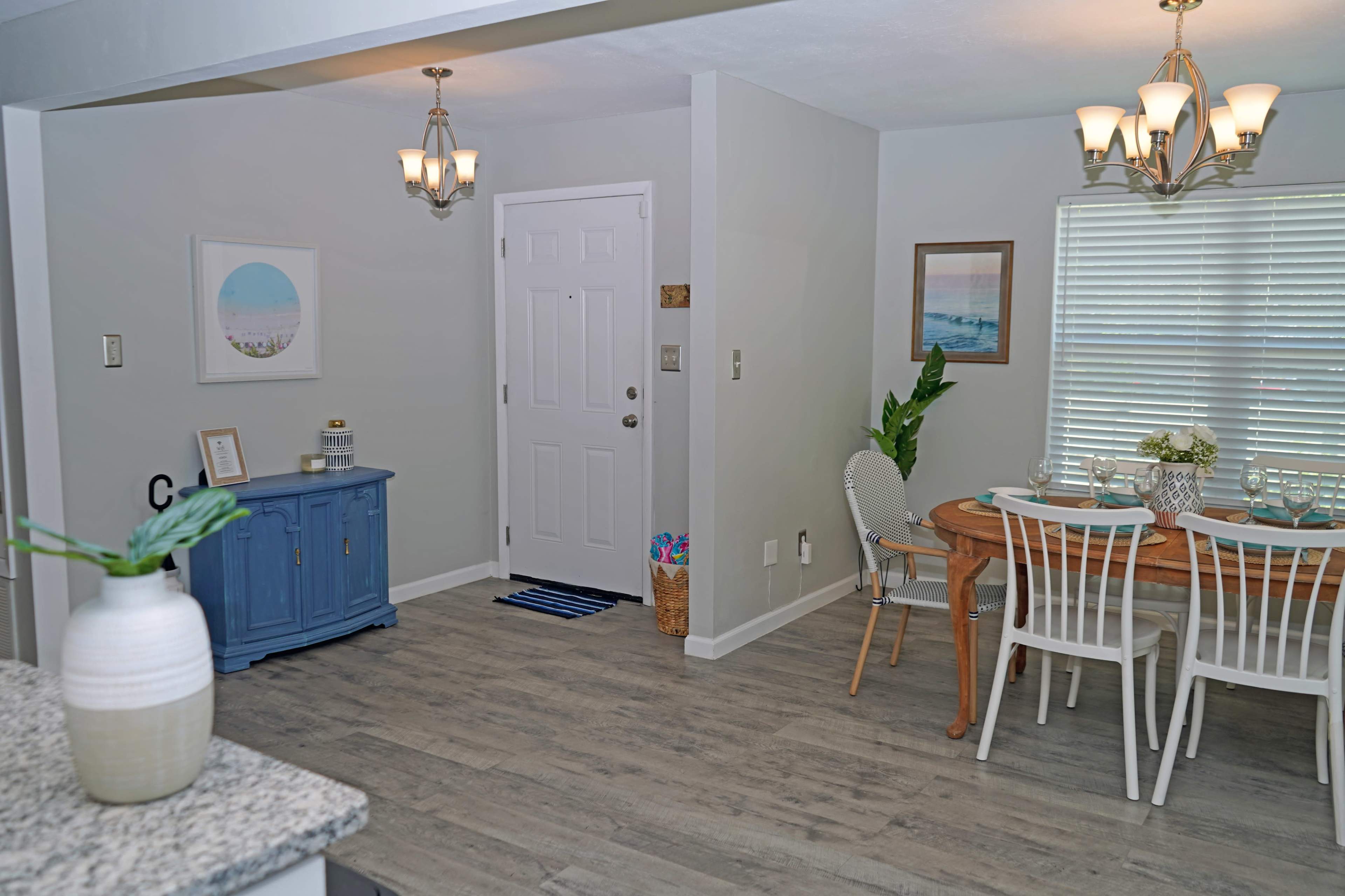 A dining area features a wooden table set with dishes, a blue cabinet, and a front door leading to the entrance.