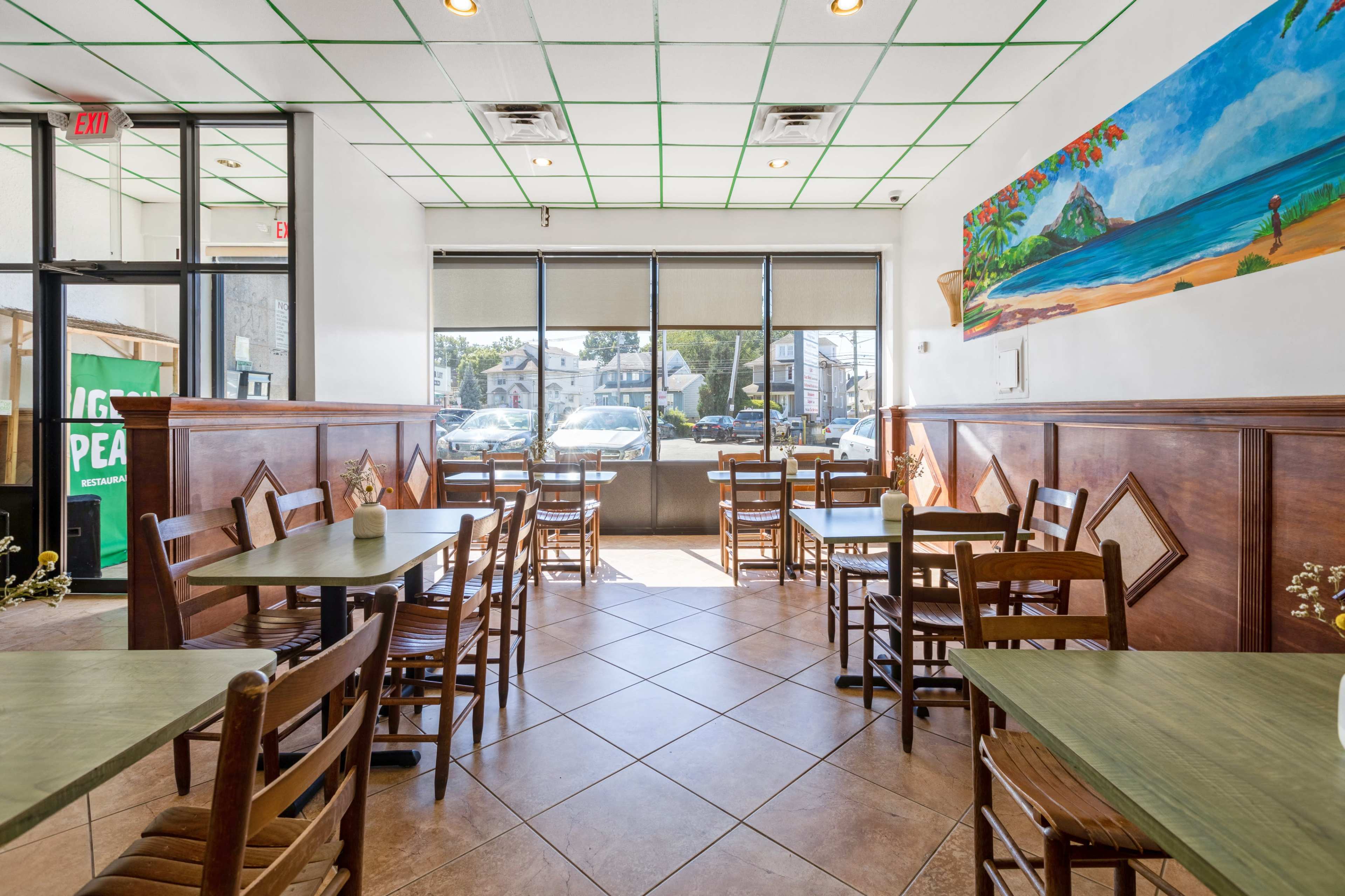 A café interior with empty tables and chairs arranged in a bright space featuring large windows and a mural of a beach scene on the wall.