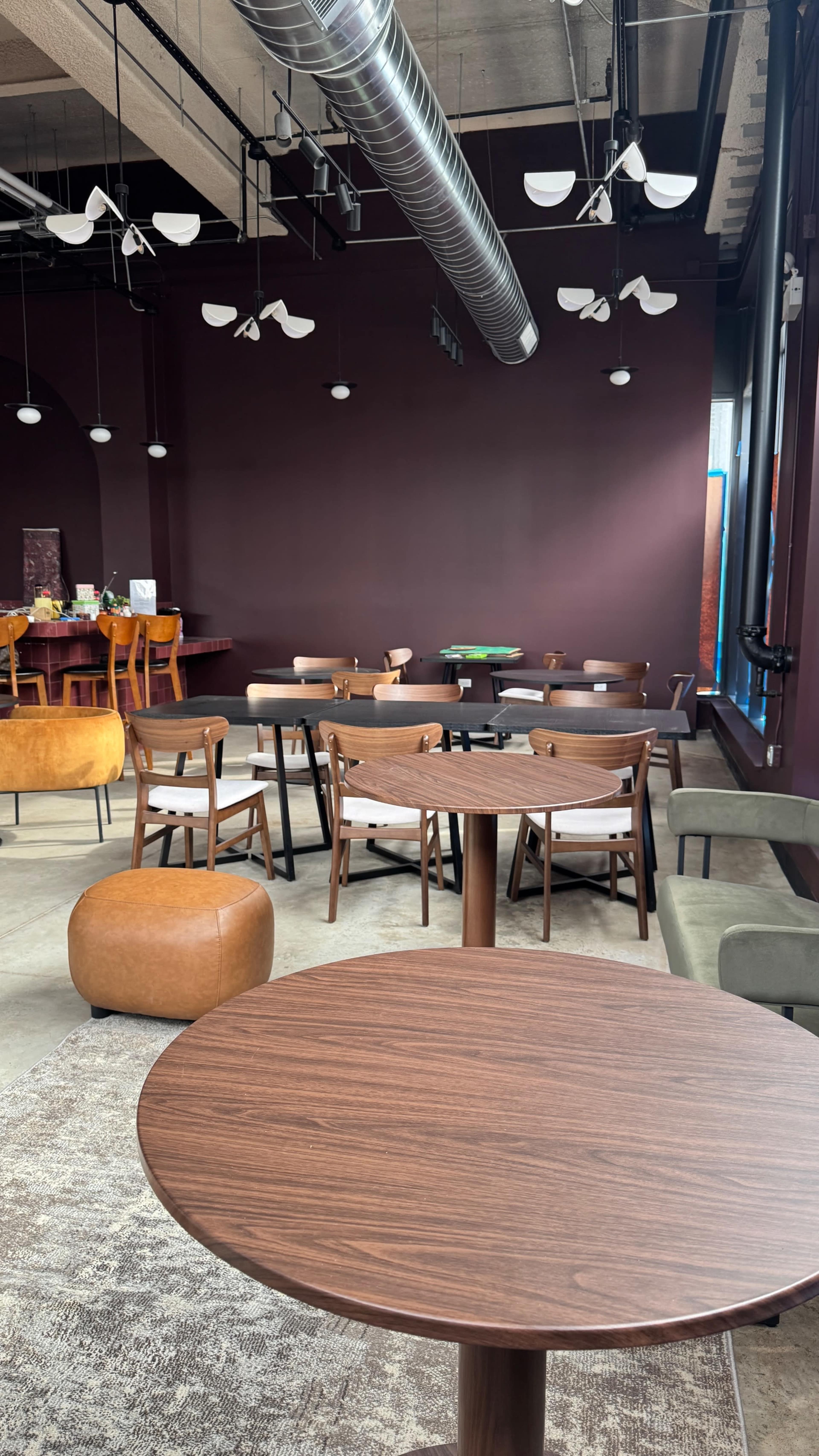 The image shows a modern café interior featuring various seating arrangements, including tables and chairs, on a concrete floor with purple walls.