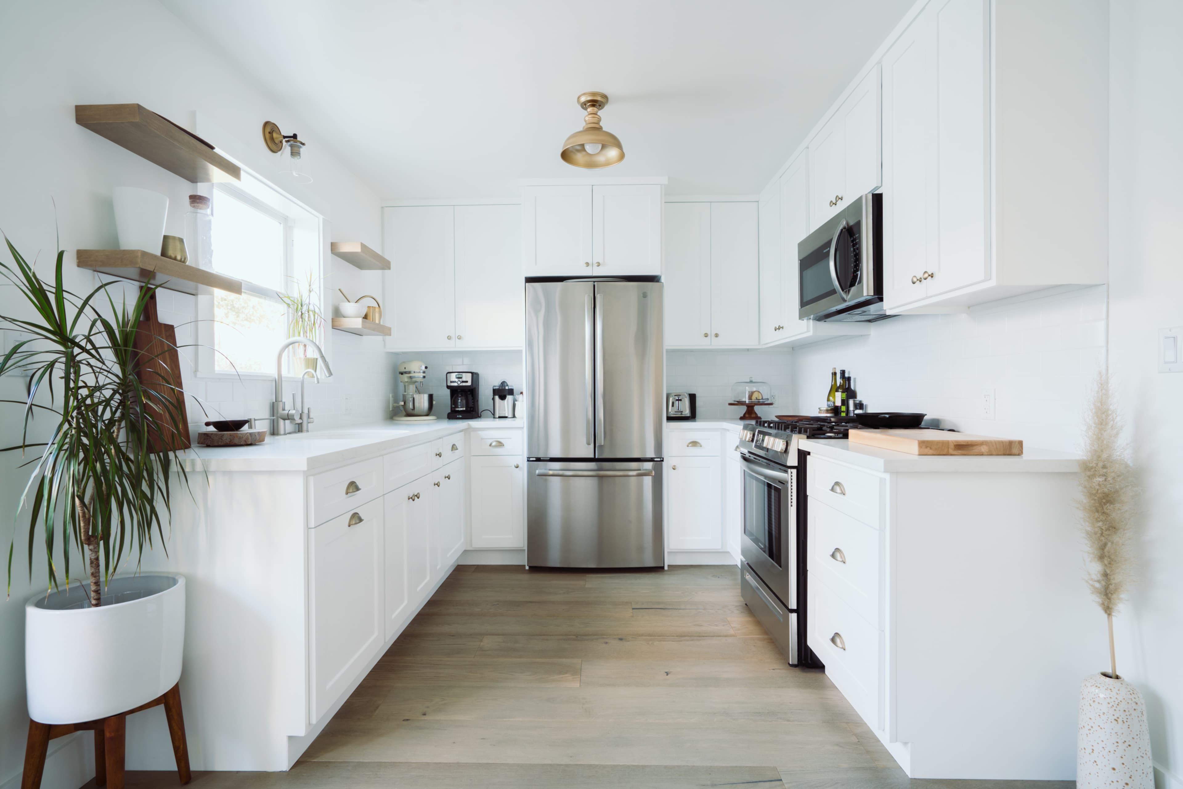 The kitchen features white cabinetry, stainless steel appliances, and wooden shelves against a light backdrop.
