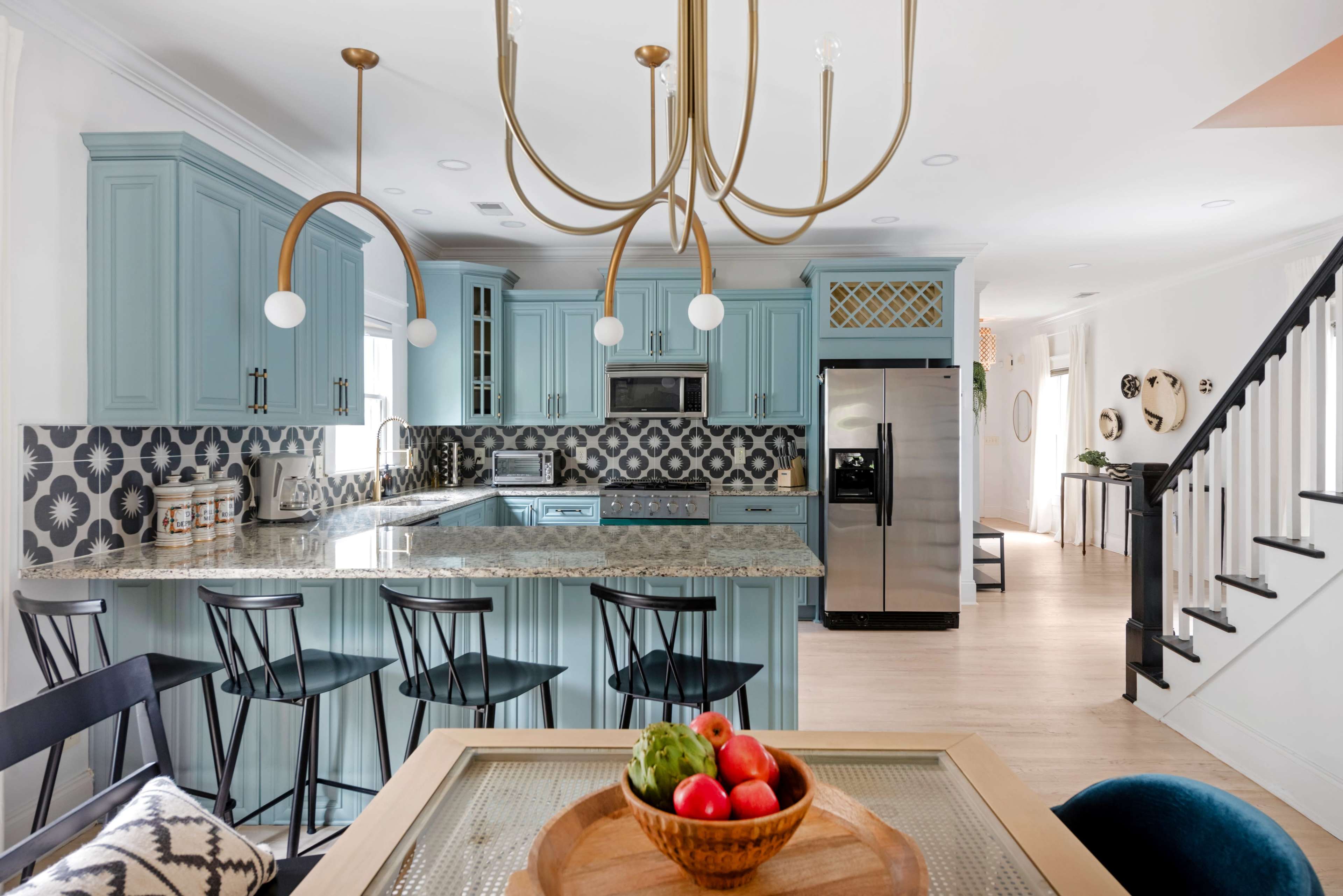The image shows a modern kitchen with light blue cabinetry, a large island, patterned tile backsplashes, and stainless steel appliances.