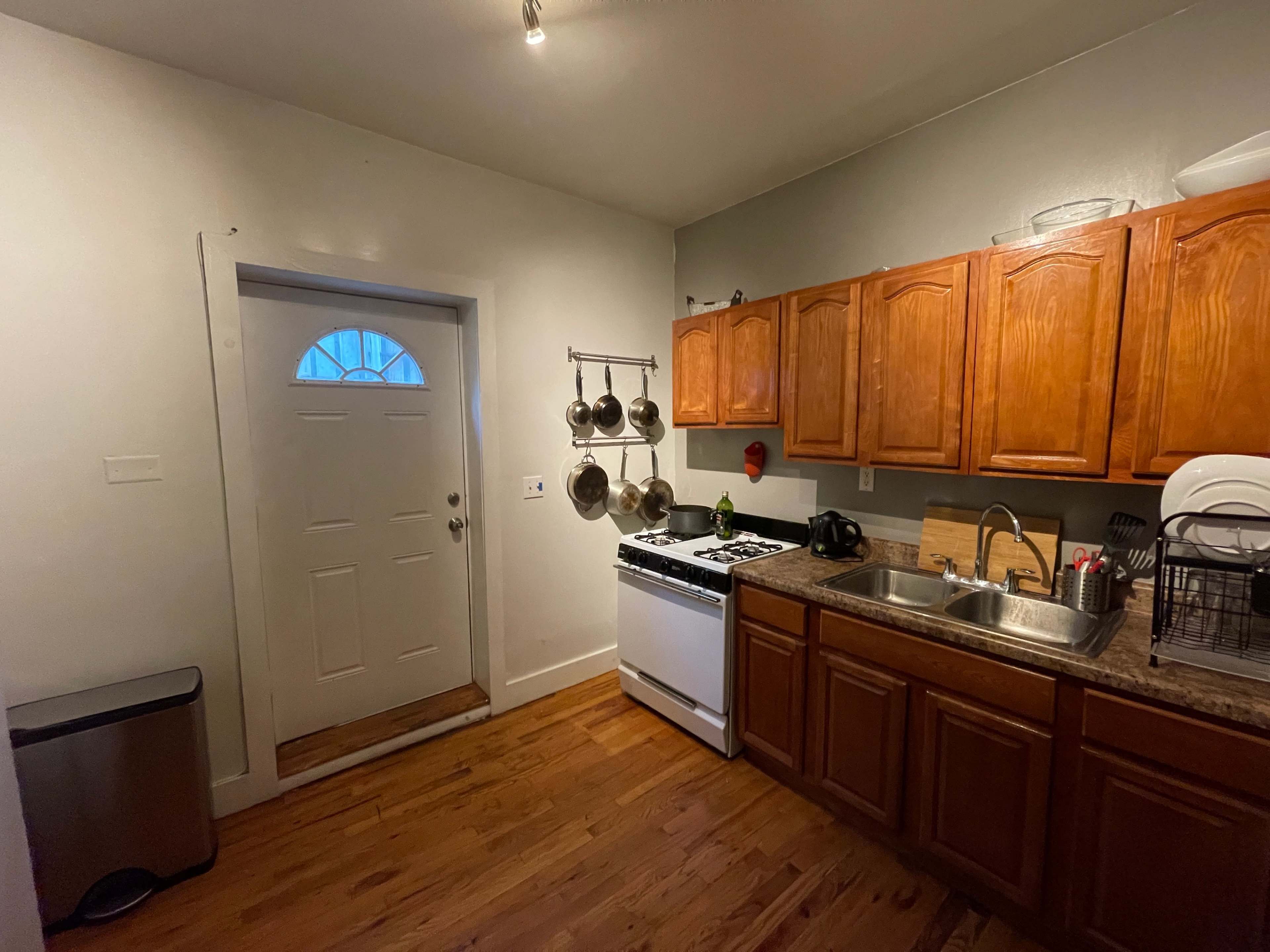 A small kitchen with wooden cabinets, a sink, a stove, and a door leading outside.
