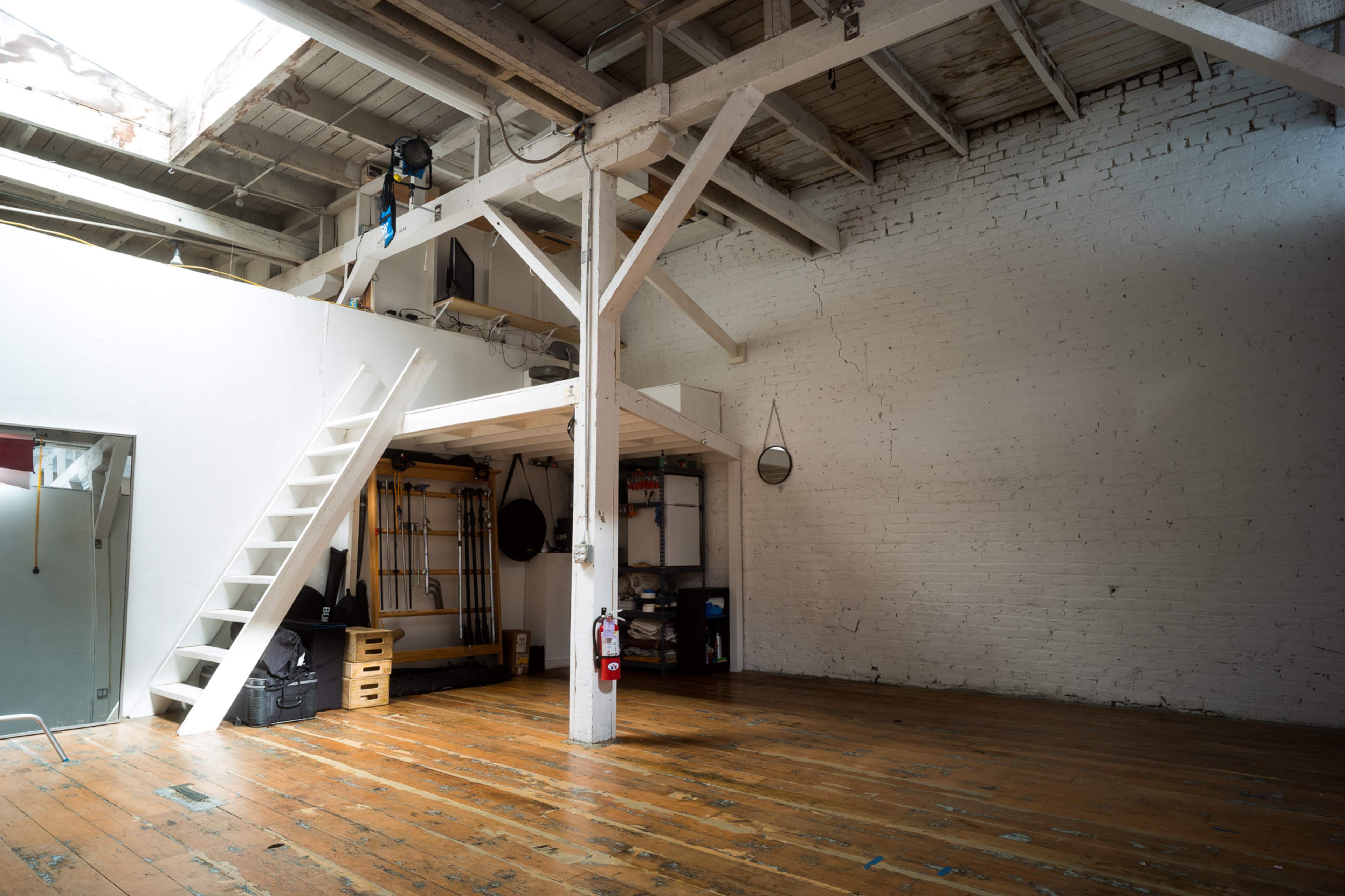 An empty room with wooden flooring, a set of stairs leading to a loft, and white-washed brick walls.