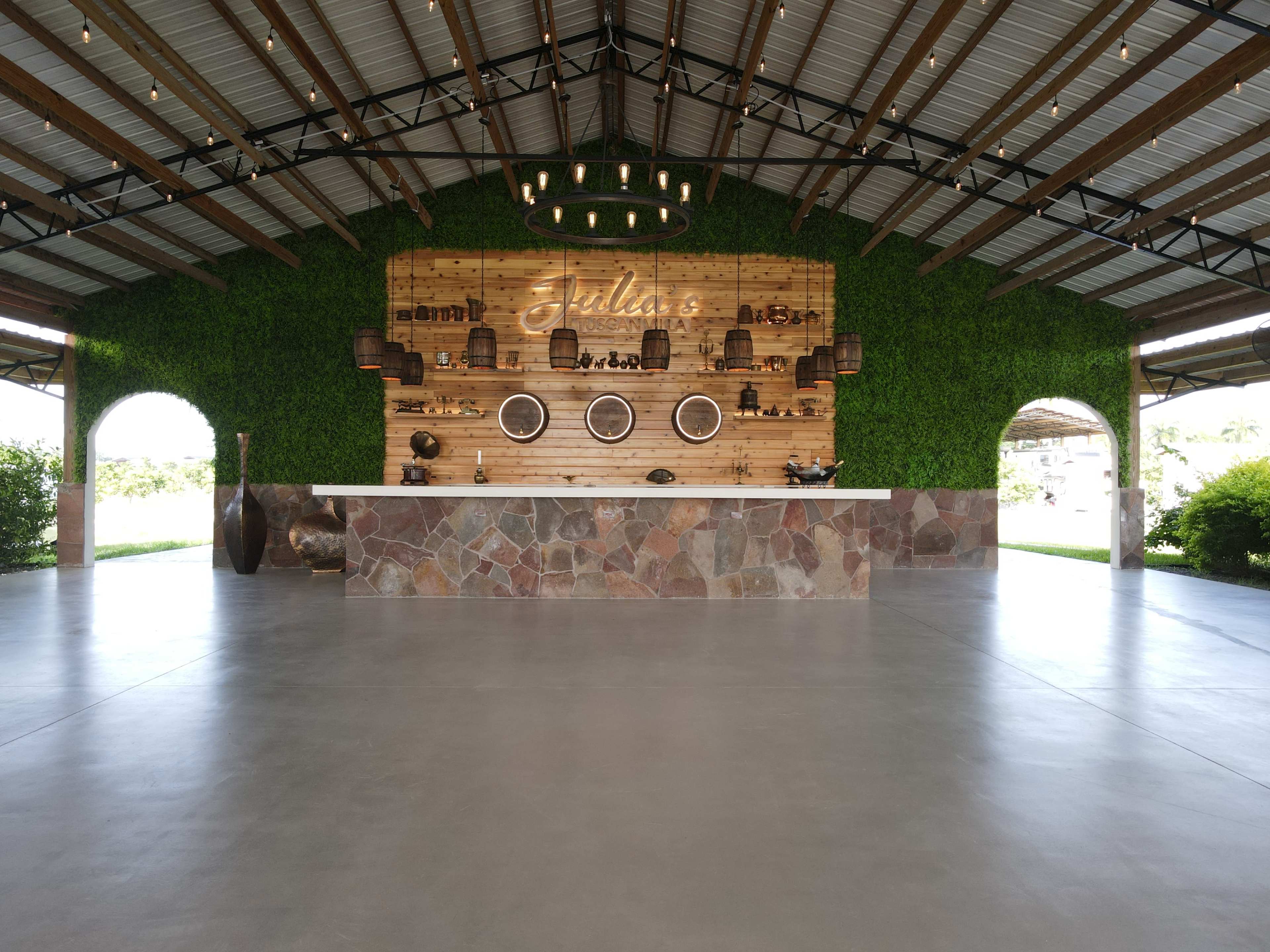 The image shows a spacious venue with a stone bar and a wall decorated with plants and shelves displaying various decorative items.
