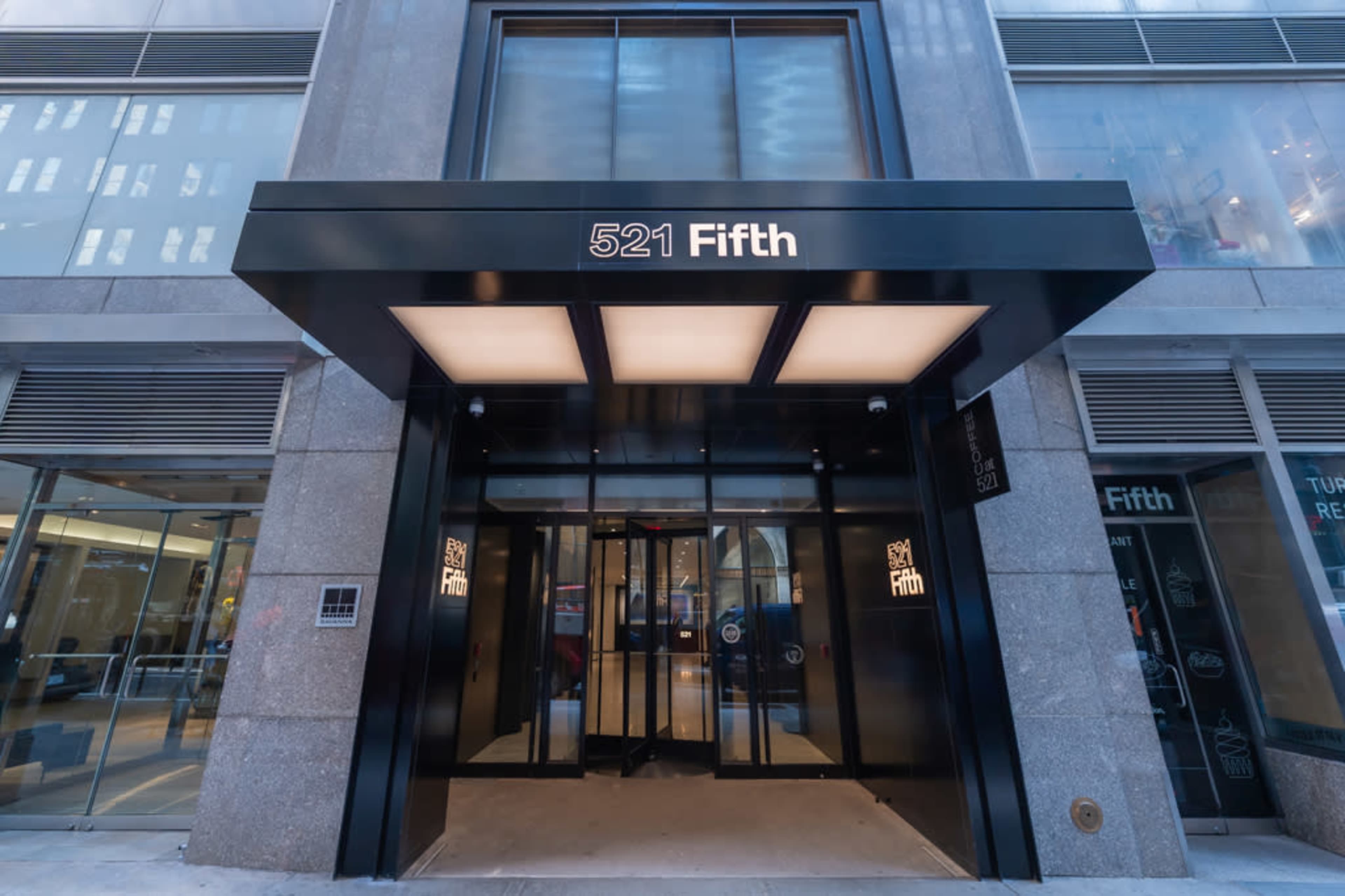 The image shows the entrance of a commercial building at 521 Fifth Avenue, featuring a black canopy and glass doors.