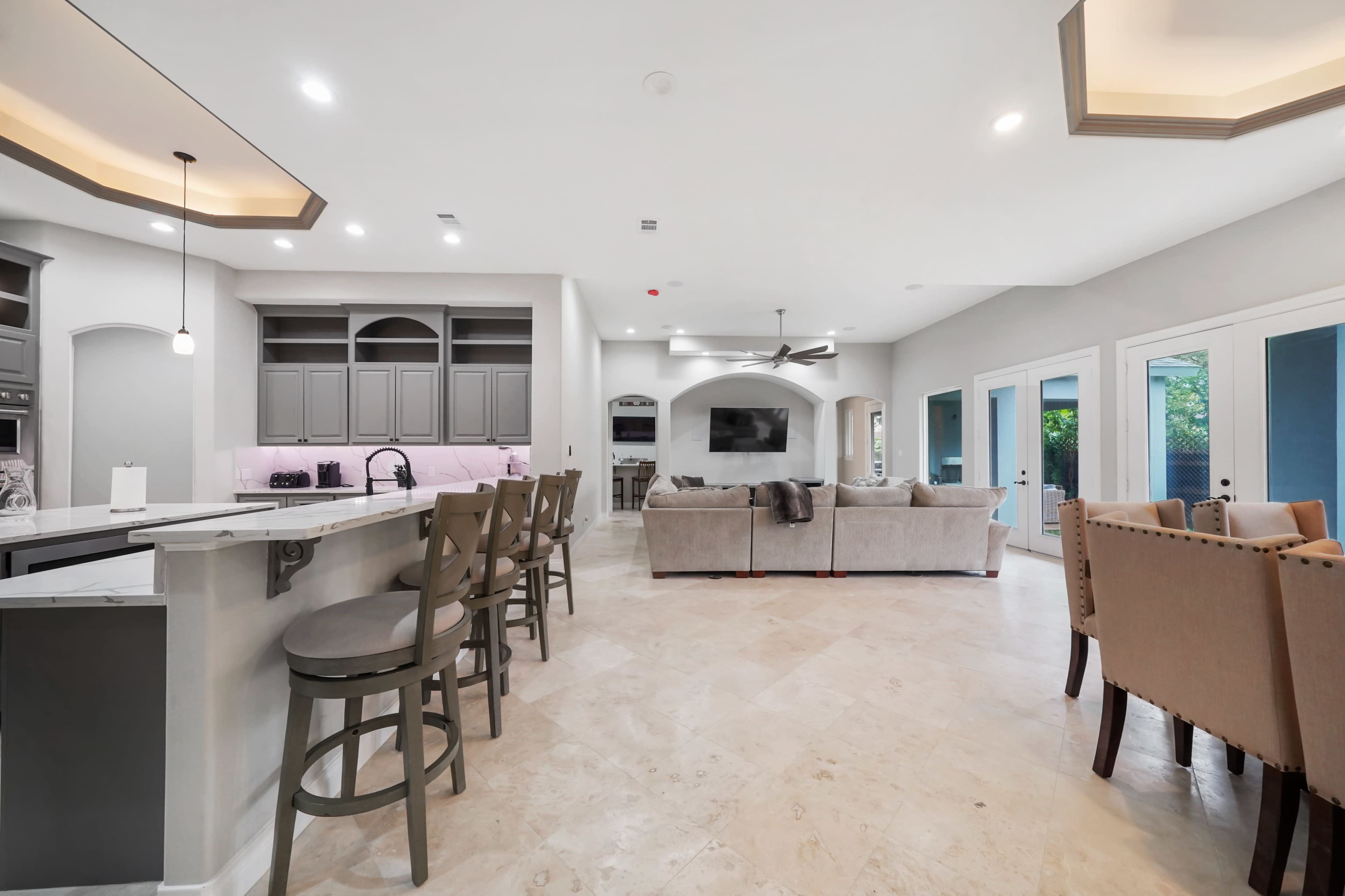 A spacious modern kitchen and living area featuring a breakfast bar, comfortable seating, and large windows allowing natural light.