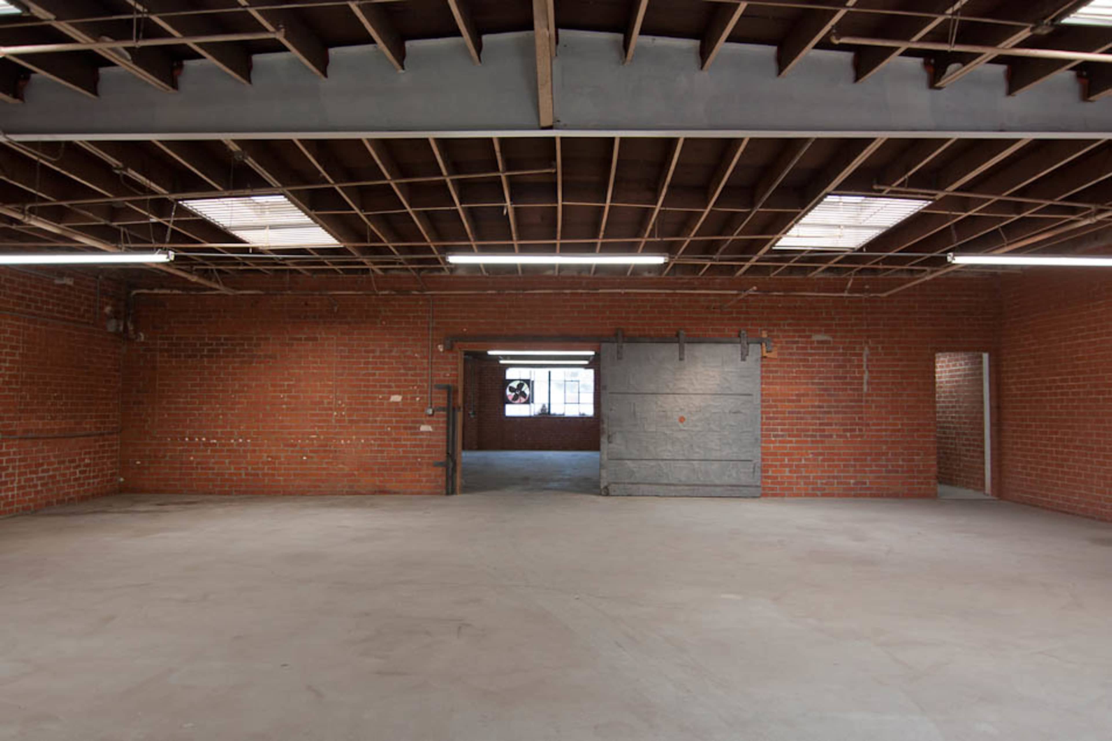 An empty industrial space with exposed brick walls, a concrete floor, and ceiling beams.