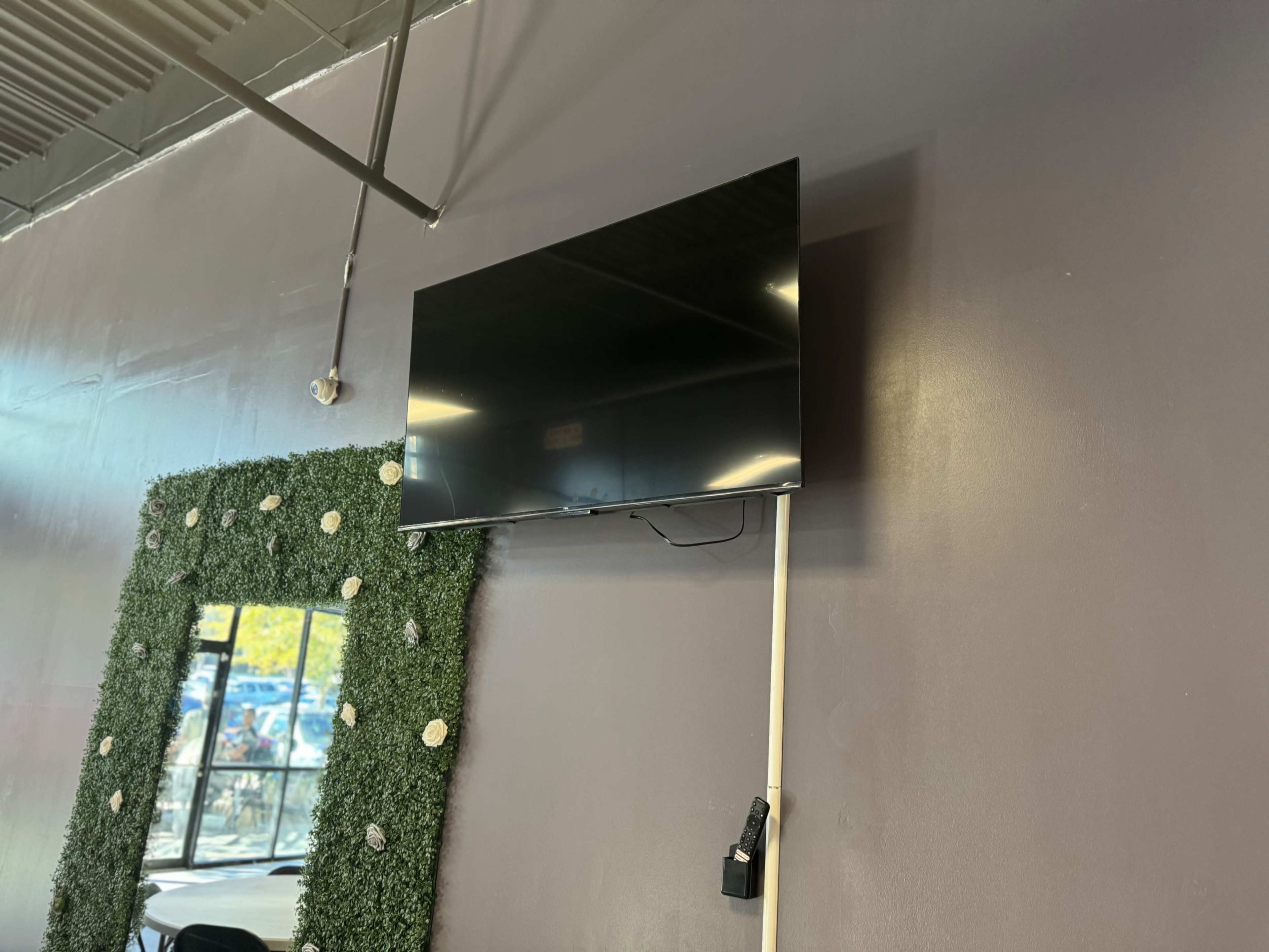 A black television is mounted on a gray wall above a green, decorative panel featuring a floral design.