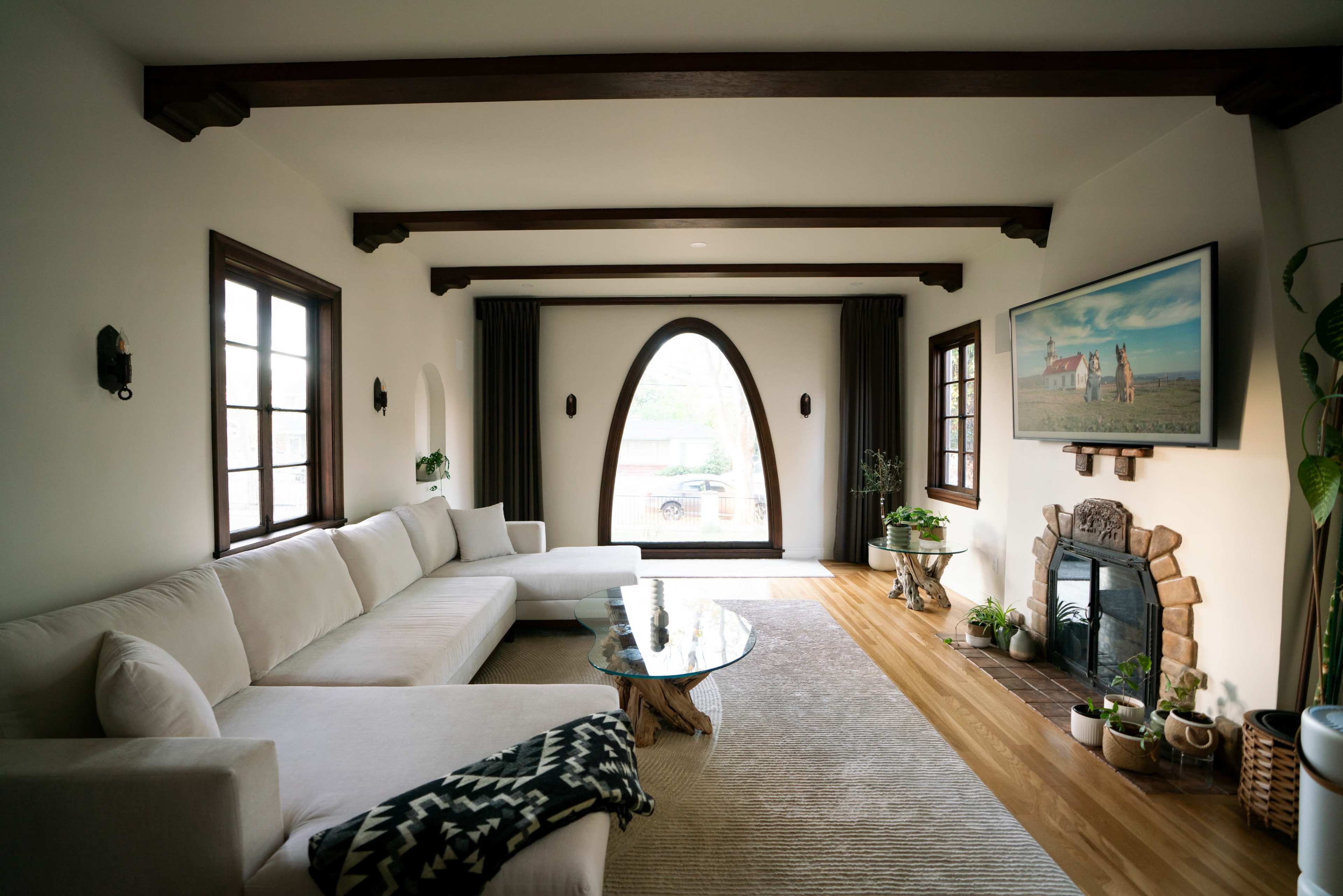 A modern living room features a large sectional couch, a glass coffee table, and an arched window with a view of the outside.
