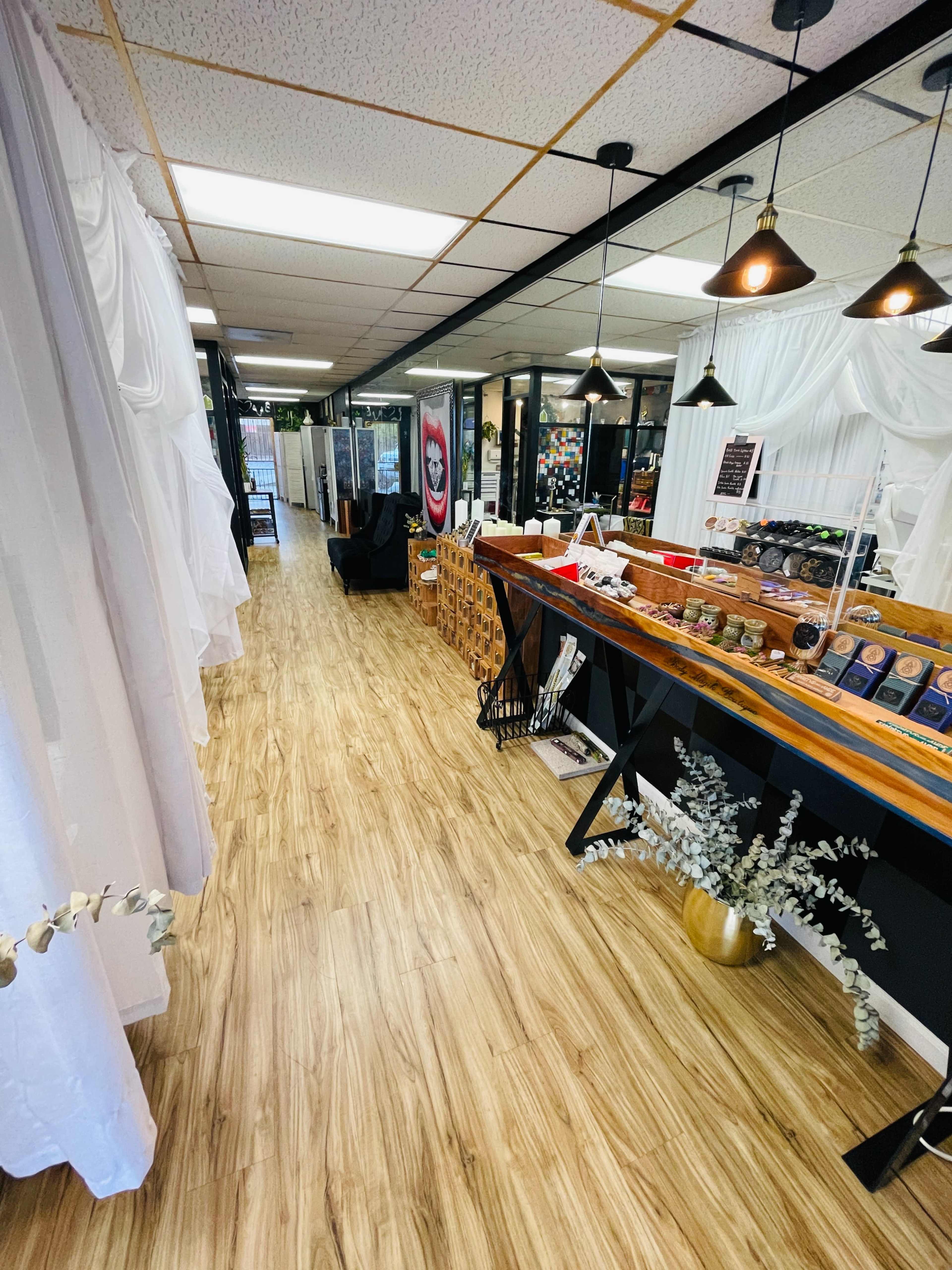 The image shows the interior of a well-organized shop with wood flooring, display tables, and a line of hanging curtains.